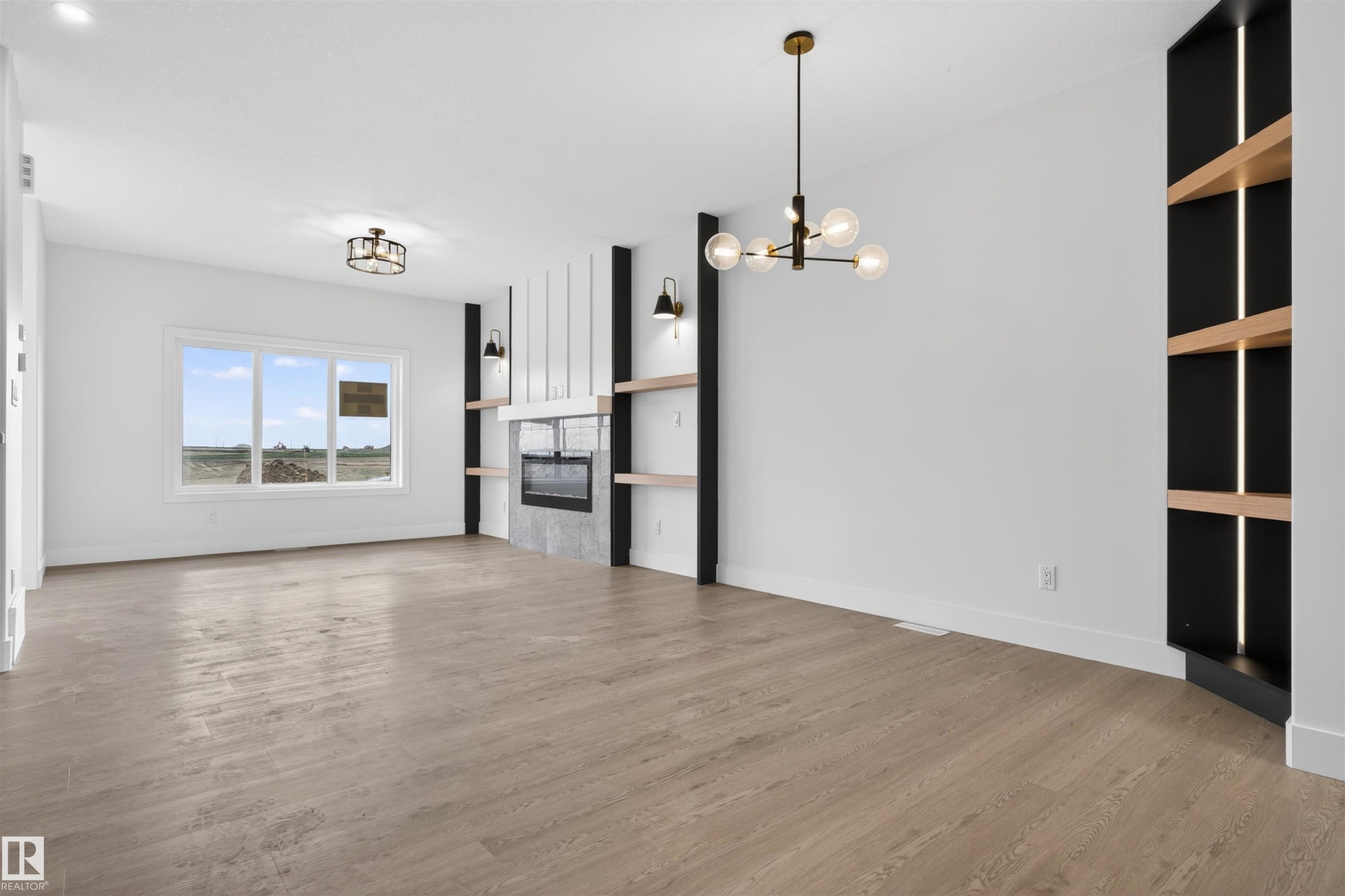 Spacious living area featuring wood-finish flooring, a contemporary fireplace with a textured surround, and a ceiling-mounted light fixture - 45 River Birch, St. Albert, AB - Indoor