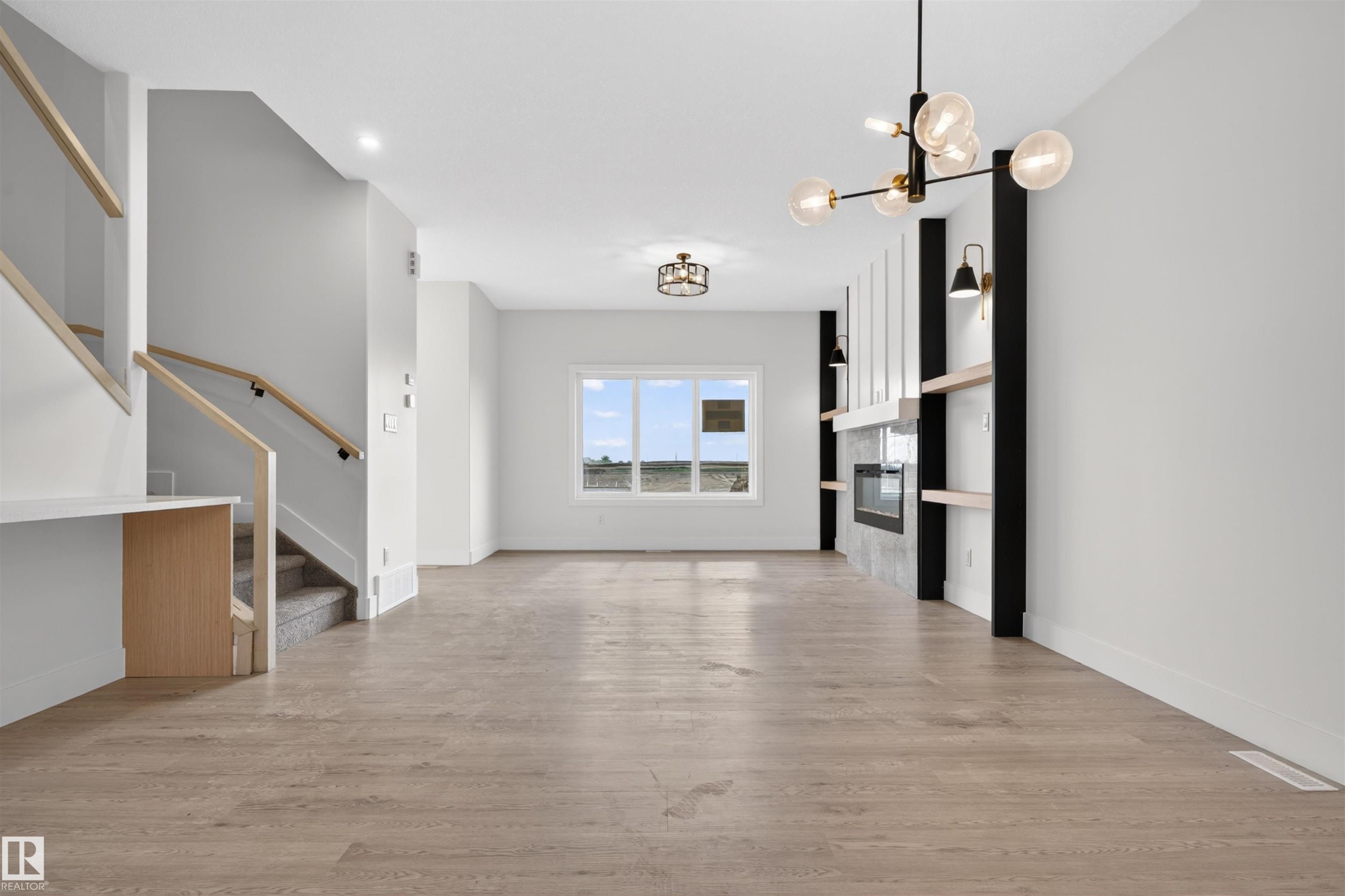 Spacious living area featuring light wood-finish flooring and a contemporary fireplace with a sleek surround and integrated shelving - 45 River Birch, St. Albert, AB - Indoor Photo Showing Other Room