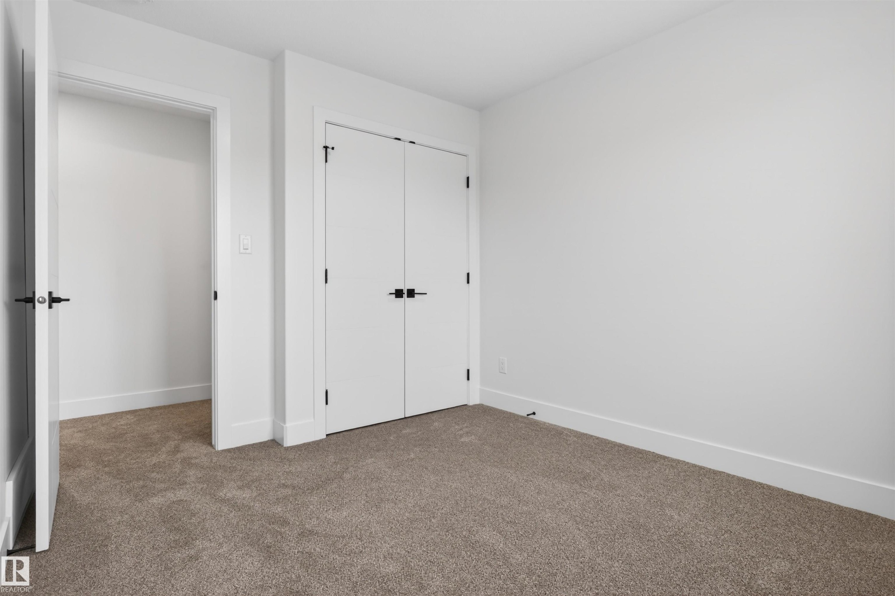 Carpeted room featuring a white interior door with black hardware, a built-in closet with double white doors and black hardware, and crisp white baseboards - 45 River Birch, St. Albert, AB - Indoor Photo Showing Other Room