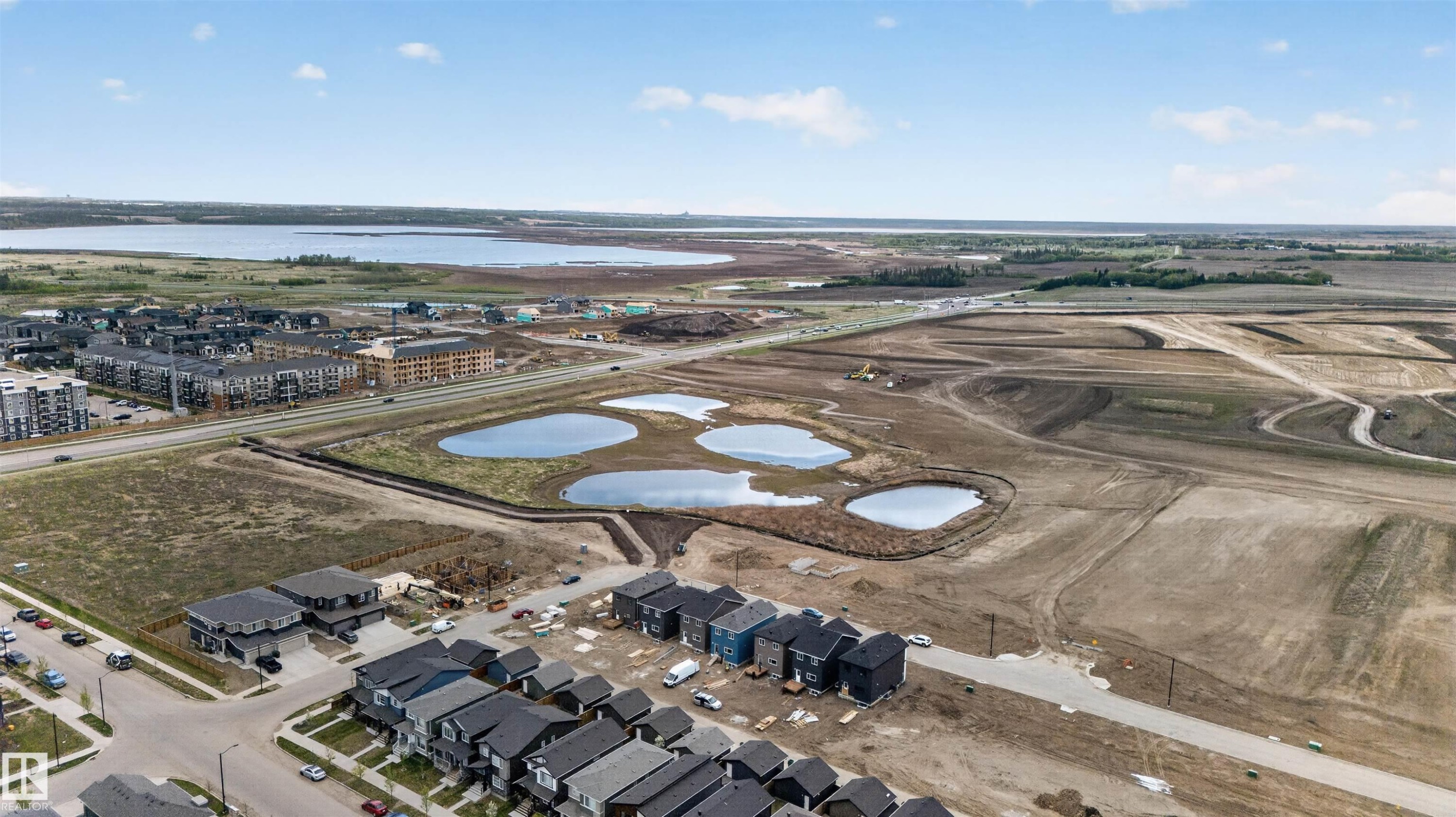 Aerial perspective of an expansive development area featuring multiple constructed residences and a large body of water in the background - 45 River Birch, St. Albert, AB - Outdoor With View