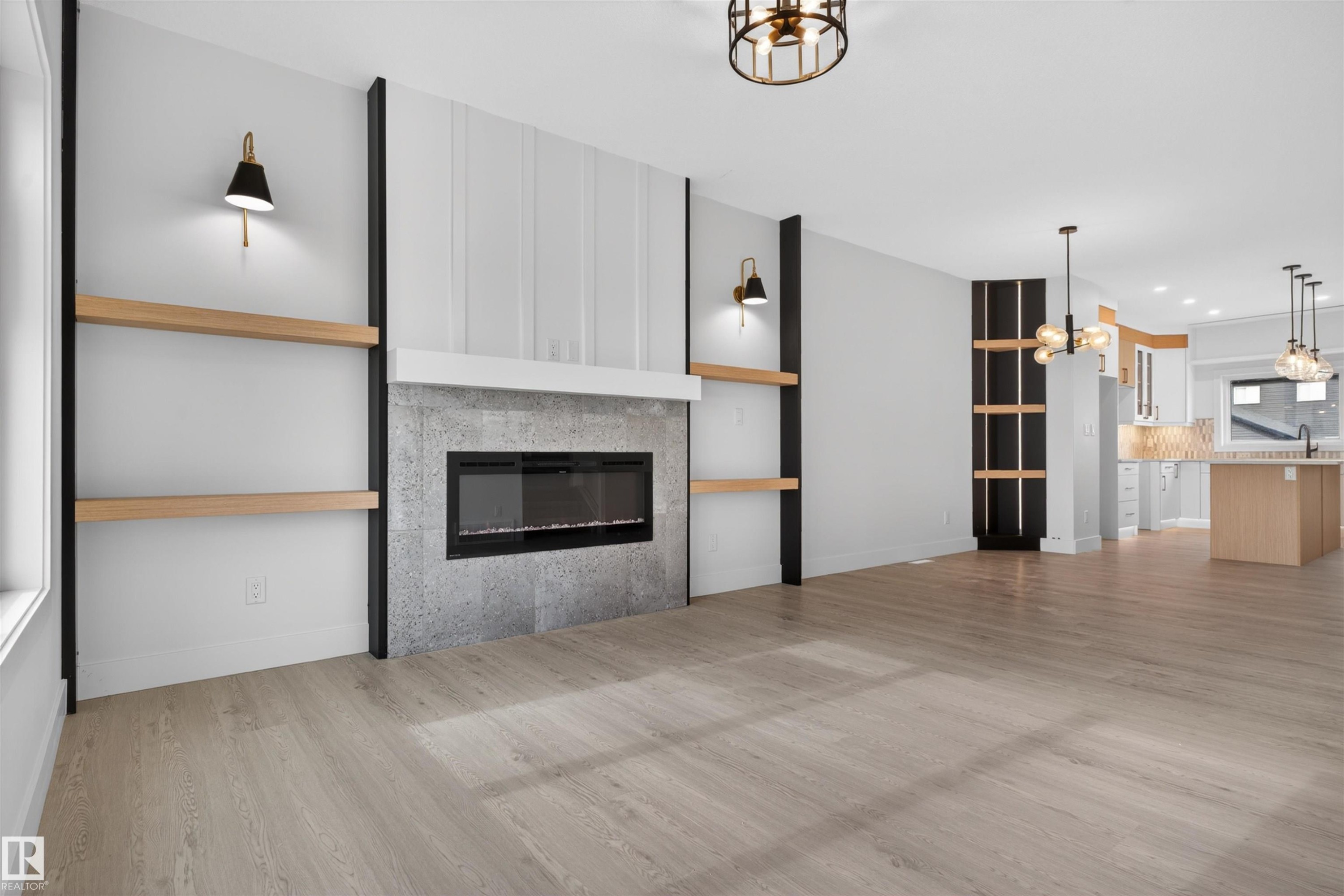 Spacious interior featuring wood-finish flooring, a linear electric fireplace with a concrete-look surround, and built-in shelving with integrated sconces - 45 River Birch, St. Albert, AB - Indoor Photo Showing Living Room With Fireplace