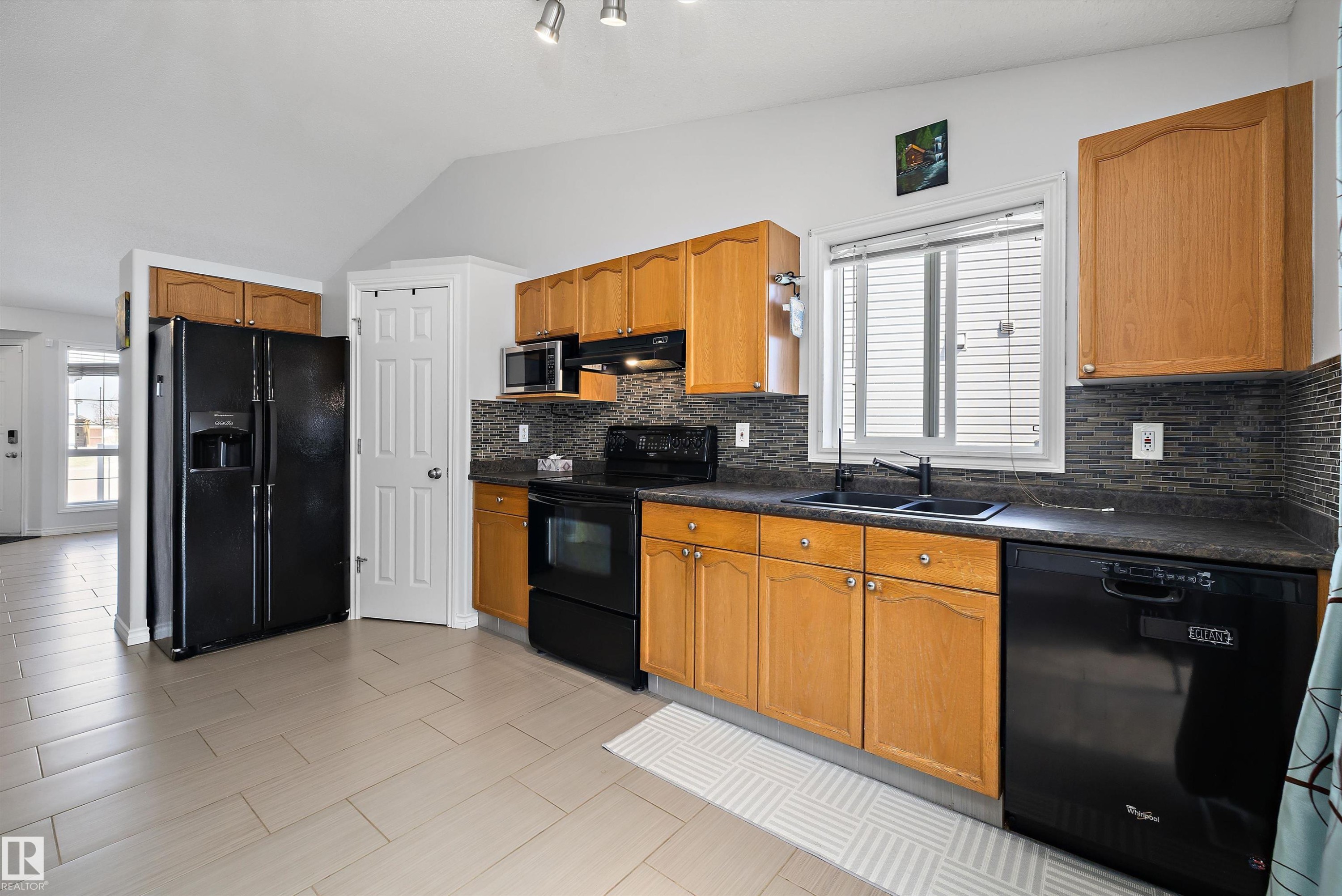 Kitchen featuring light wood cabinetry, dark countertops, and a mosaic tile backsplash - 1811 37 Avenue, Edmonton, AB - Indoor Photo Showing Kitchen With Double Sink