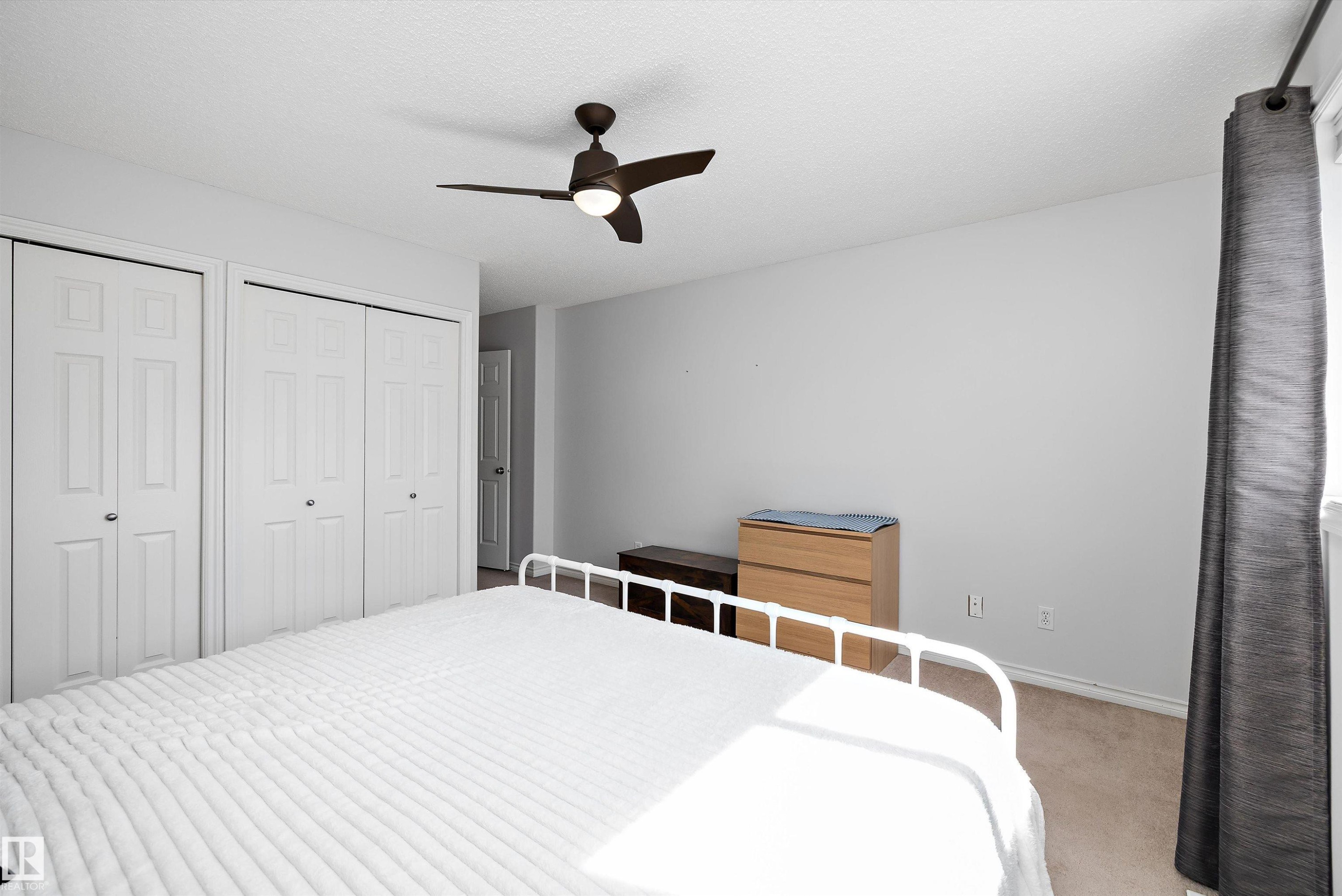 Bedroom featuring a ceiling fan with integrated lighting, two bi-fold panel door closets, light grey wall paint, and a window with dark curtain rod - 1811 37 Avenue, Edmonton, AB - Indoor Photo Showing Bedroom