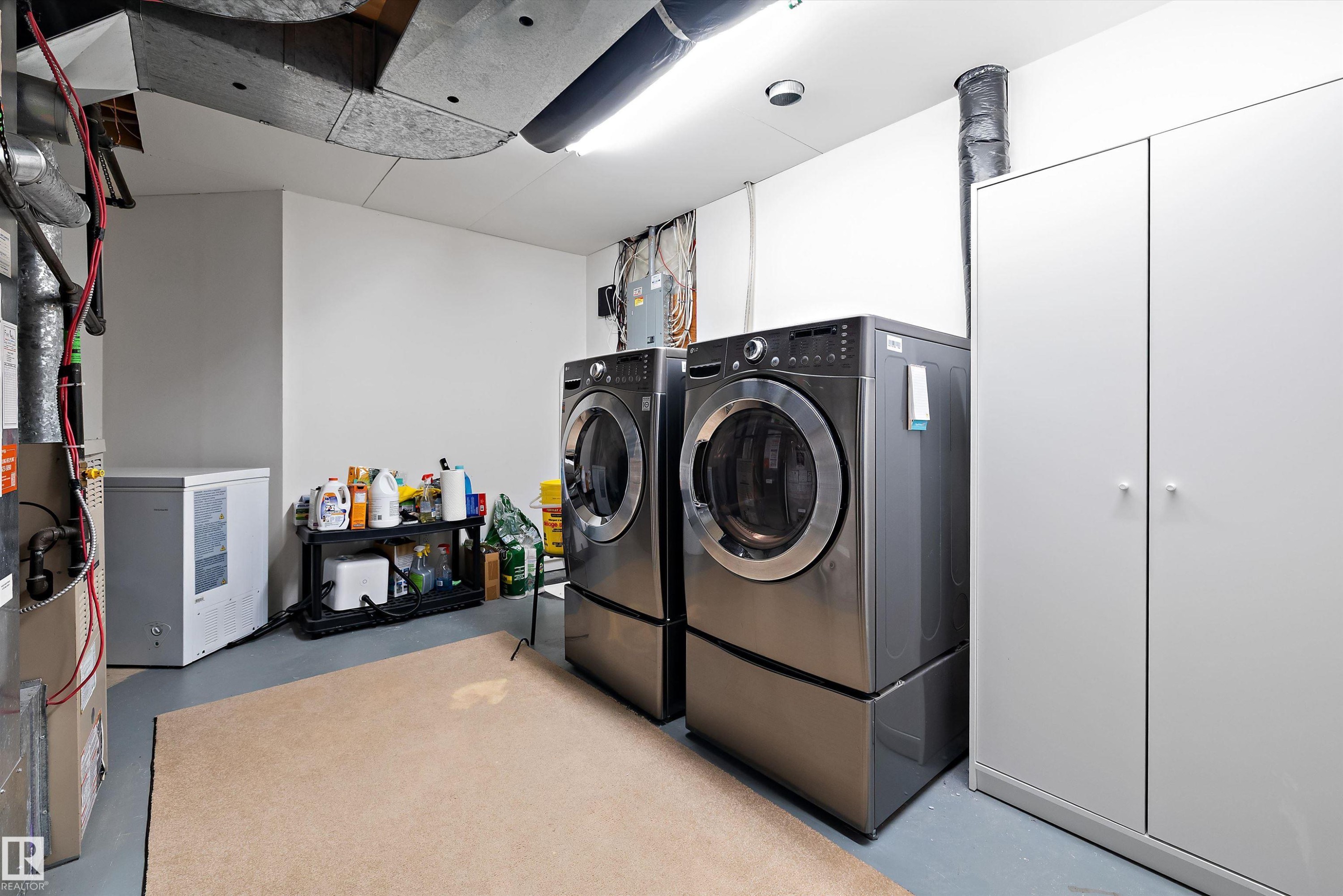 Dedicated utility space featuring dual front-loading laundry machines on pedestals, a white storage cabinet, and overhead fluorescent lighting - 1811 37 Avenue, Edmonton, AB - Indoor Photo Showing Laundry Room
