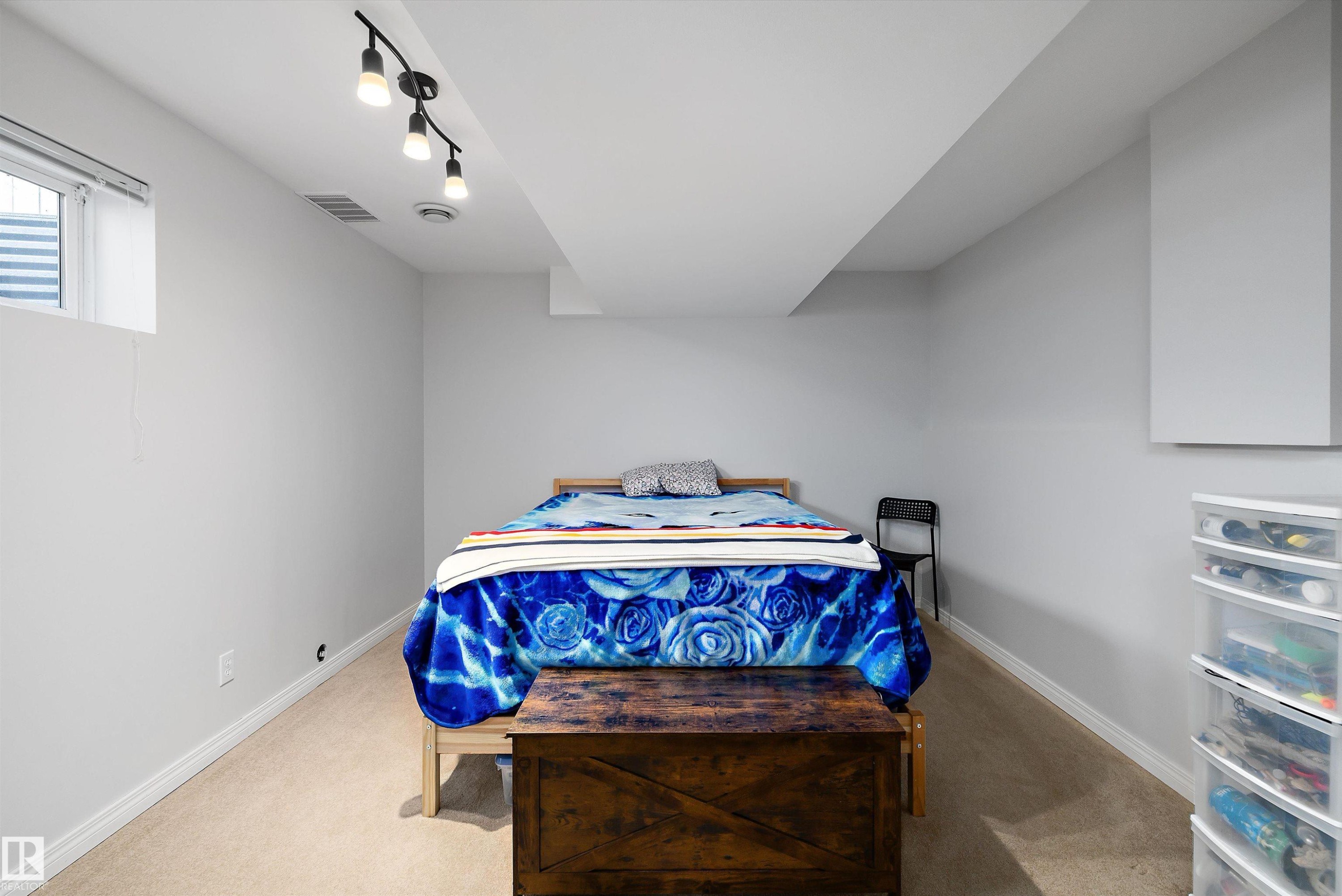 Carpeted room with a ceiling-mounted track light fixture, egress window, white baseboards, and neutral wall paint - 1811 37 Avenue, Edmonton, AB - Indoor Photo Showing Bedroom