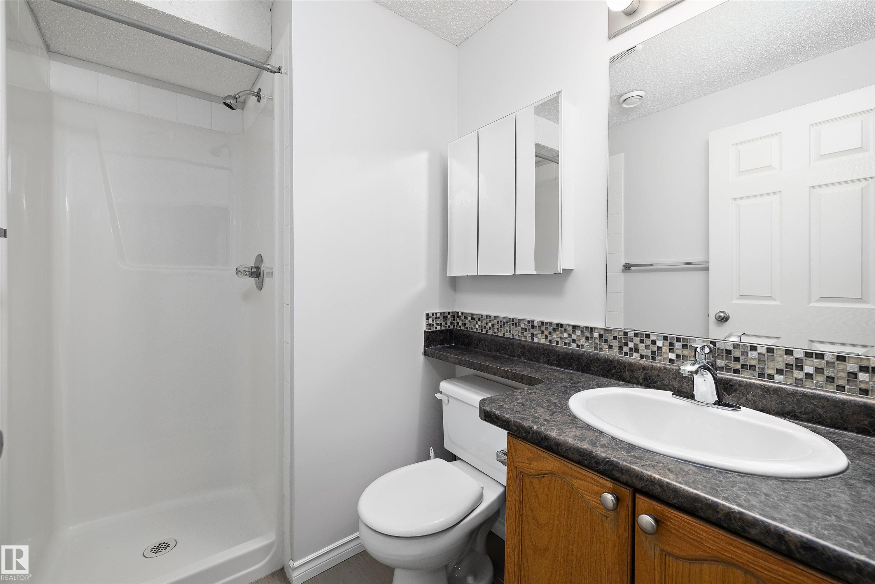 Bathroom featuring a fiberglass shower stall, mosaic tile backsplash, countertop with integrated sink, wood-finish vanity, and medicine cabinet - 1811 37 Avenue, Edmonton, AB - Indoor Photo Showing Bathroom