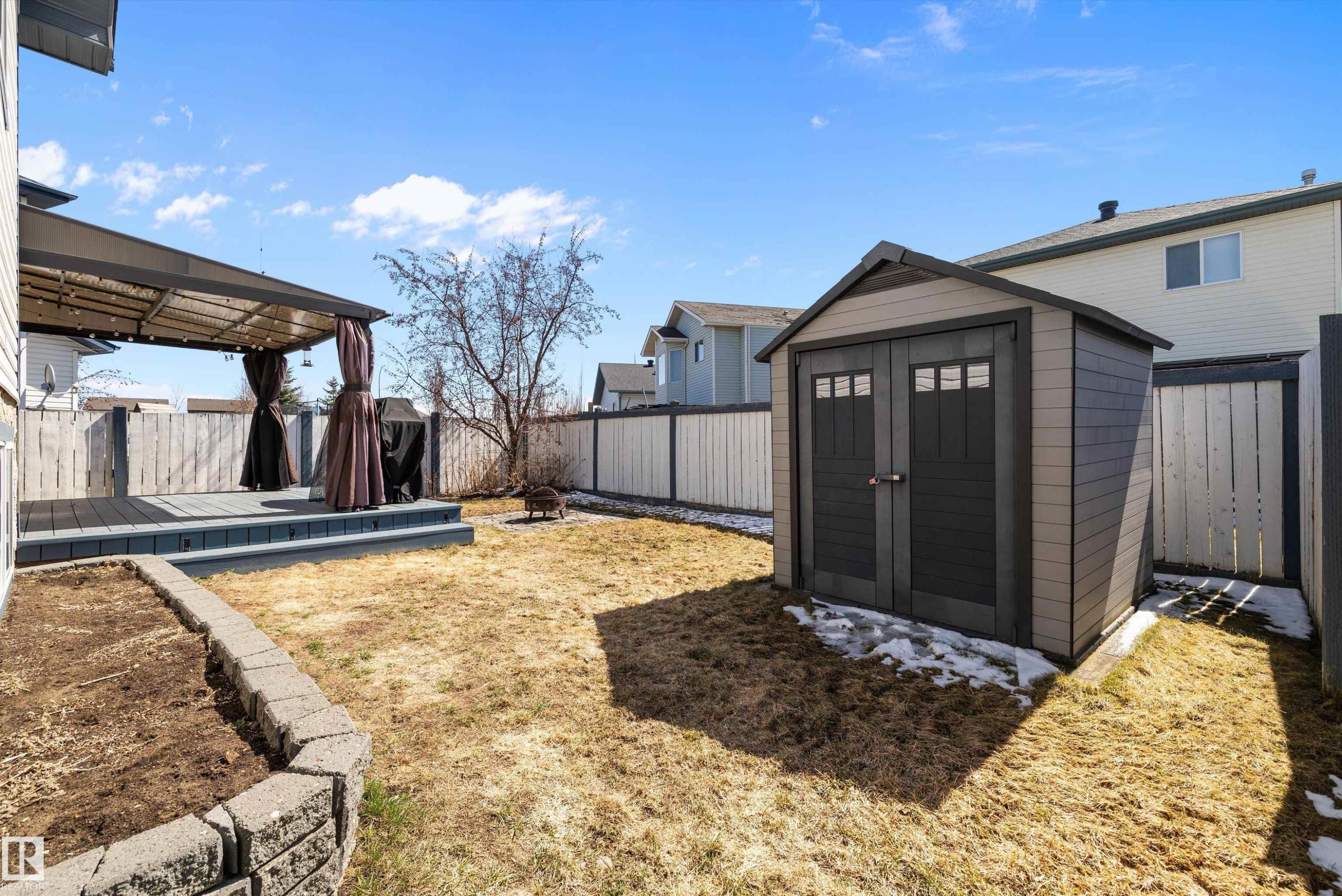 Spacious backyard featuring a multi-level deck with a privacy pergola, a dedicated garden bed with stone retaining wall, and a multi-purpose storage shed - 1811 37 Avenue, Edmonton, AB - Outdoor With Exterior