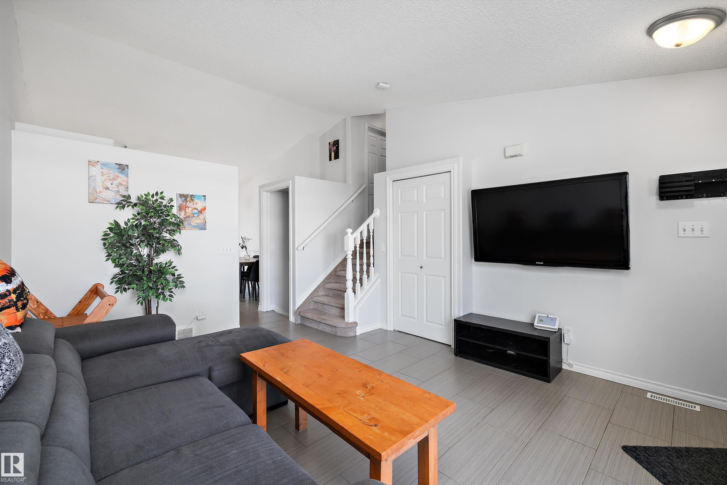 Open-concept living space featuring wood-finish flooring, a wall-mounted television, and a white bi-fold closet door - 1811 37 Avenue, Edmonton, AB - Indoor Photo Showing Living Room
