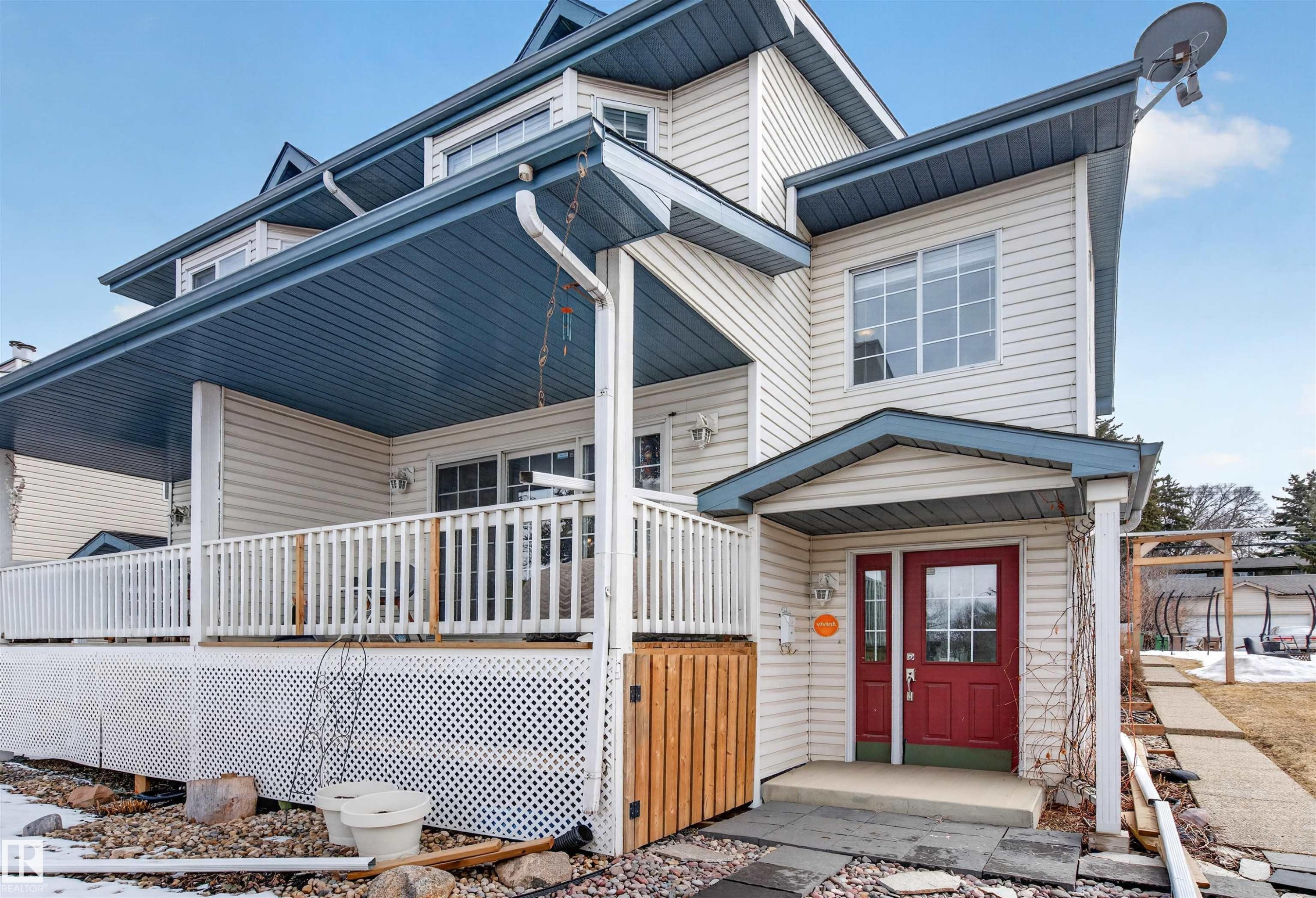 This property features light-colored siding, a covered porch with a white railing, and a red front door - 2 Sturgeon Road, St. Albert, AB - Outdoor With Deck Patio Veranda