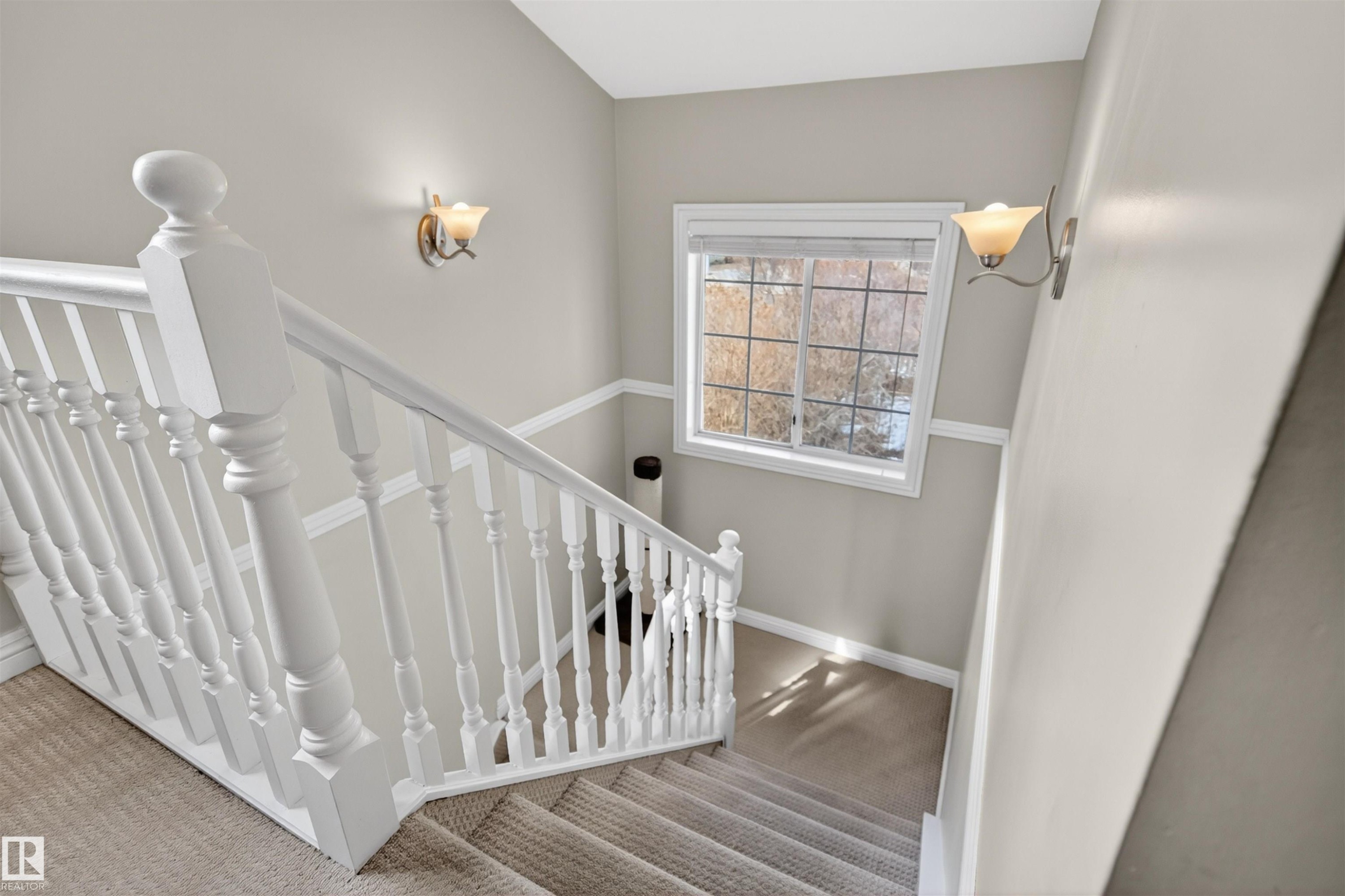 Carpeted staircase with white balusters and handrail, featuring a window and wall sconces providing illumination - 2 Sturgeon Road, St. Albert, AB - Indoor Photo Showing Other Room