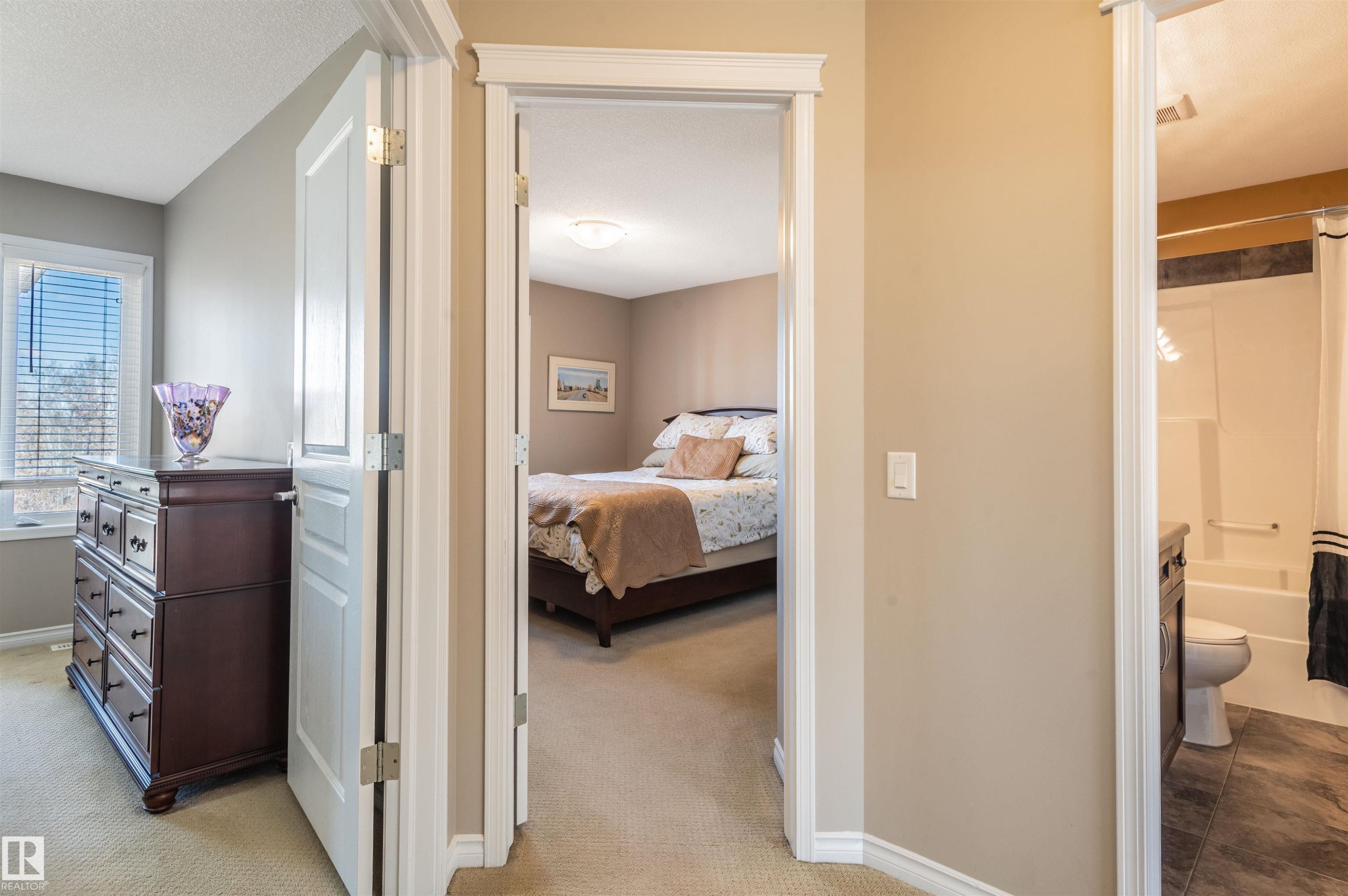 Bright hallway with light beige walls and white trim, featuring an open doorway to a carpeted room with a window and a second open doorway to a bathroom with tile flooring and a white tub-shower combination - 121 Ellington Crescent, St. Albert, AB - Indoor