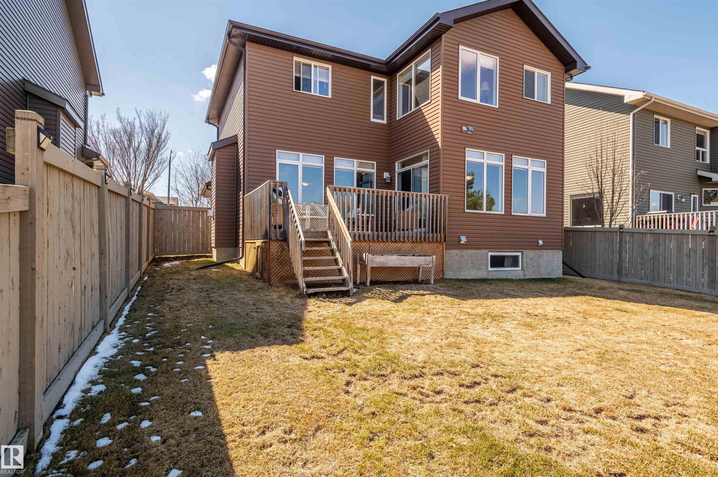 Spacious backyard featuring a wooden deck with stairs, brown siding, multiple large windows, and full perimeter fencing - 121 Ellington Crescent, St. Albert, AB - Outdoor With Exterior