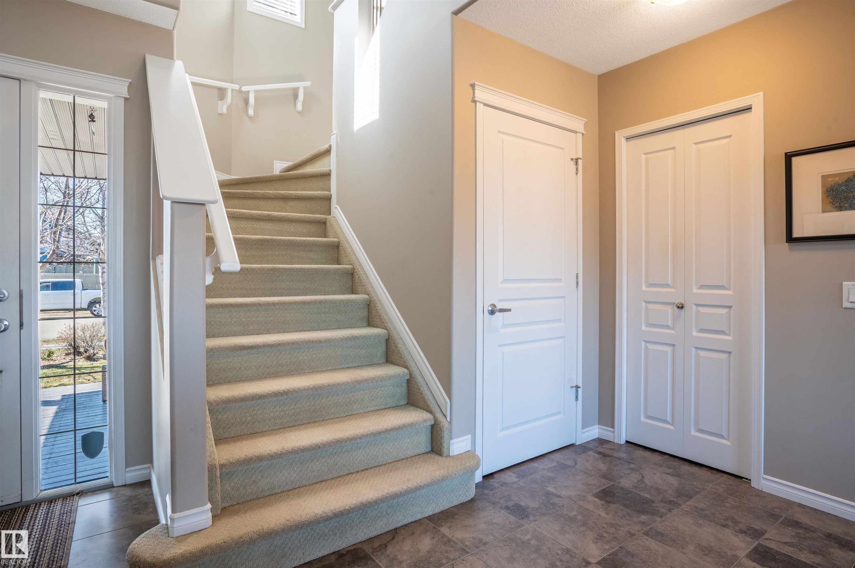 Entryway featuring a carpeted staircase with white railings, a front door with decorative glass inserts, and a tiled floor - 121 Ellington Crescent, St. Albert, AB - Indoor Photo Showing Other Room