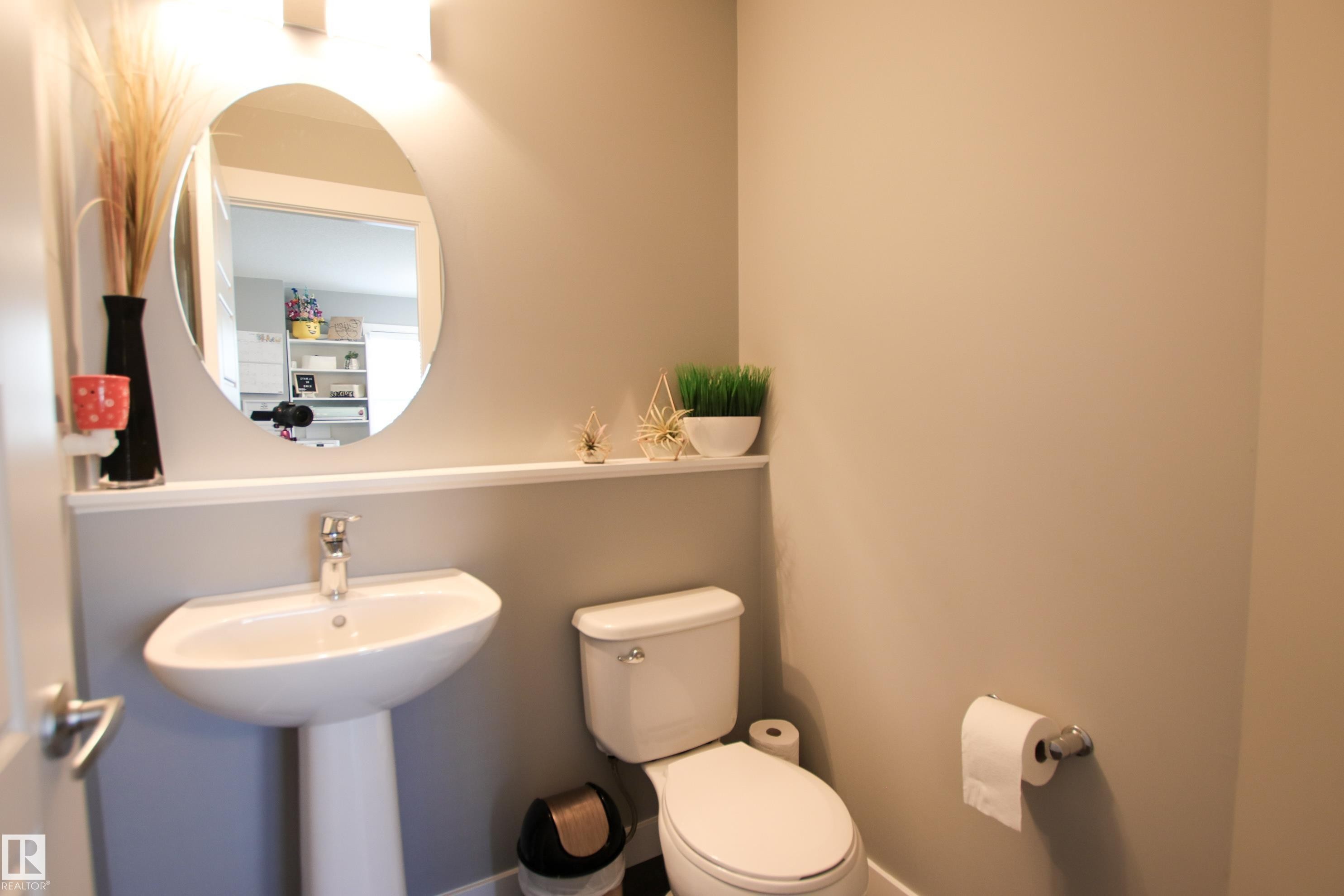 Pedestal sink with chrome faucet, oval mirror, and wall-mounted lighting - 3805 170A Avenue, Edmonton, AB - Indoor Photo Showing Bathroom
