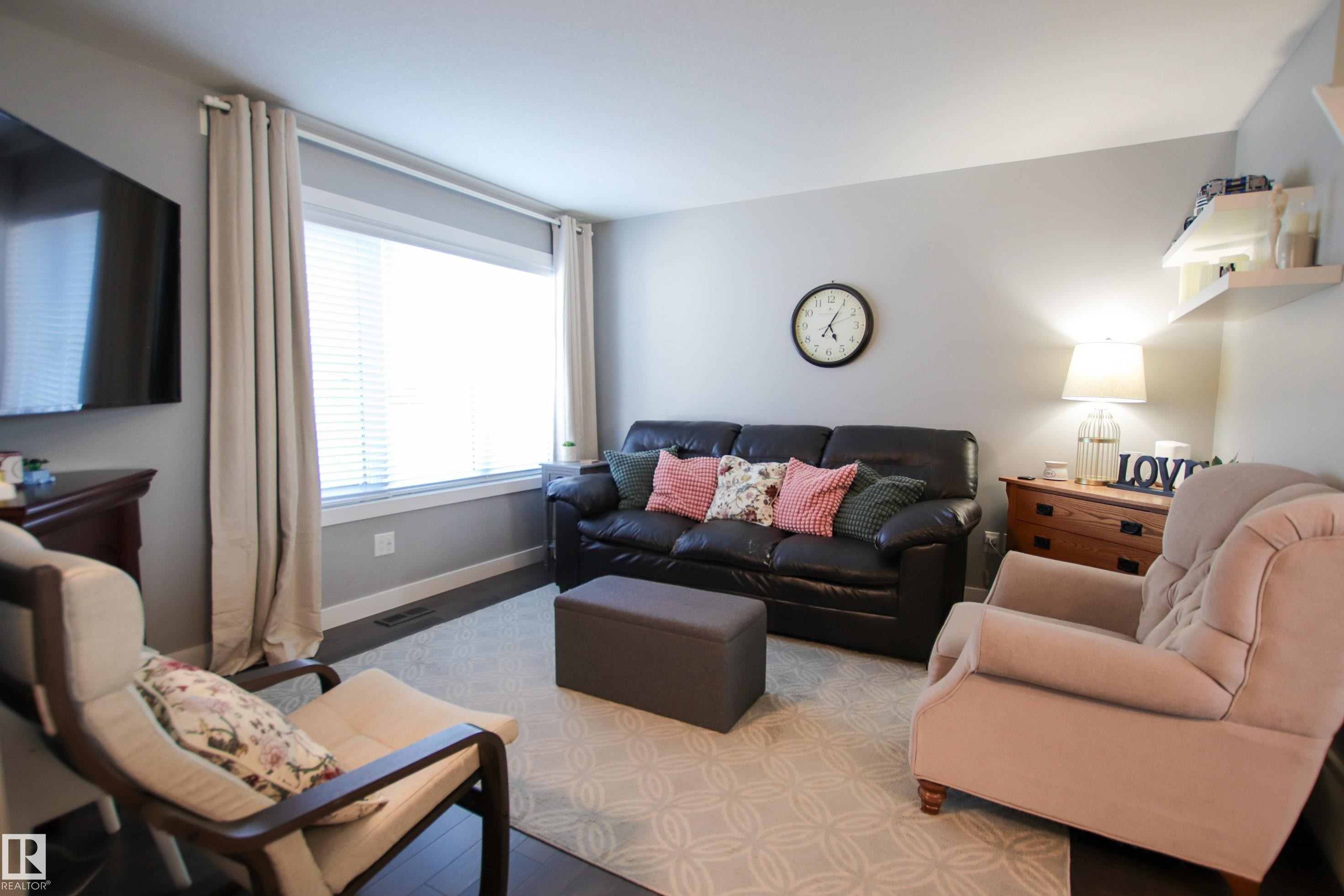 Inviting living area featuring dark wood-finish flooring, a large window with blinds and drapes, and light gray wall paint - 3805 170A Avenue, Edmonton, AB - Indoor Photo Showing Living Room
