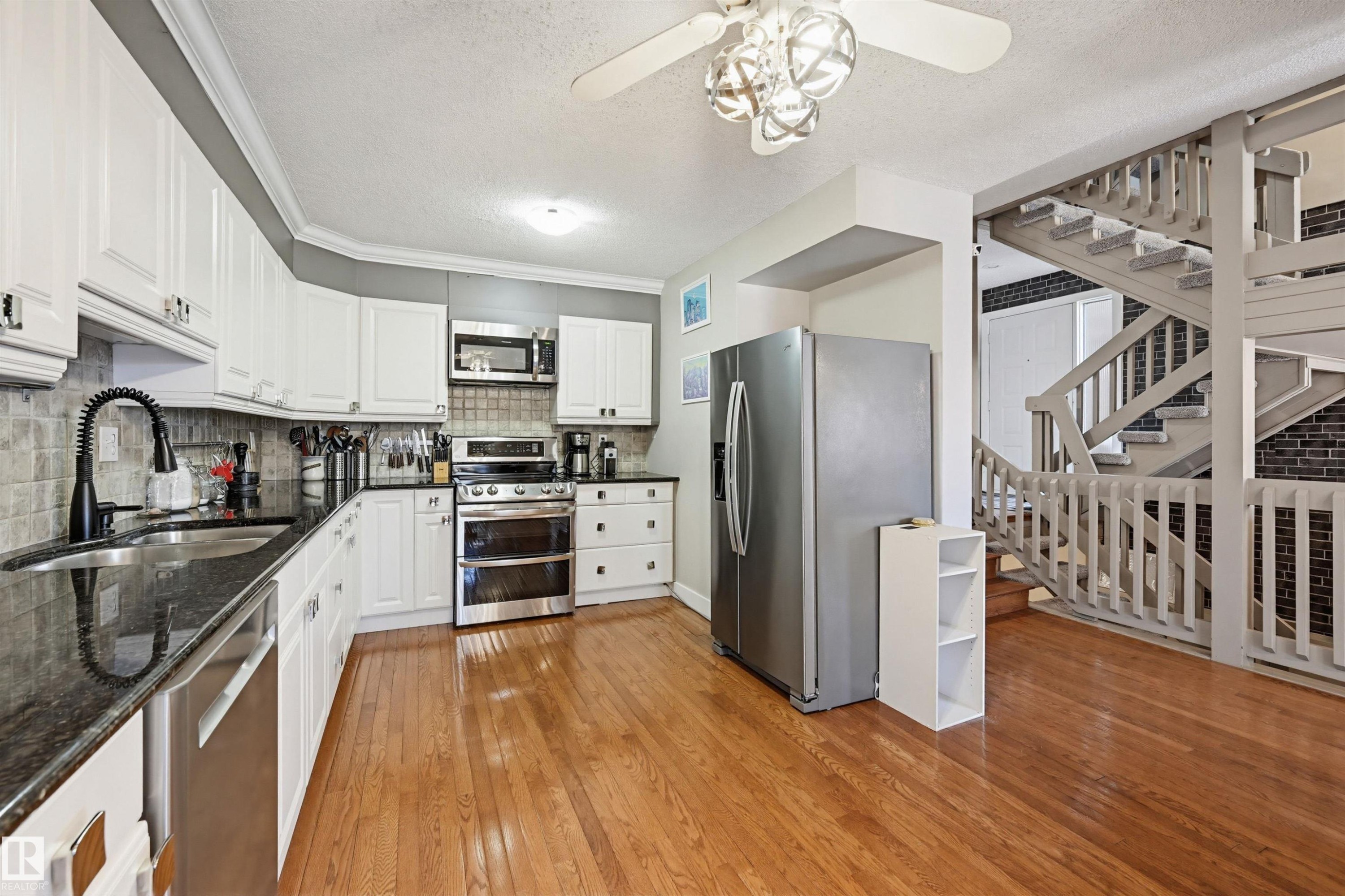 Kitchen featuring wood-finish flooring, white cabinetry, dark countertops, and a full suite of stainless steel appliances - 139 Wolf Willow Crescent, Edmonton, AB - Indoor Photo Showing Kitchen With Double Sink