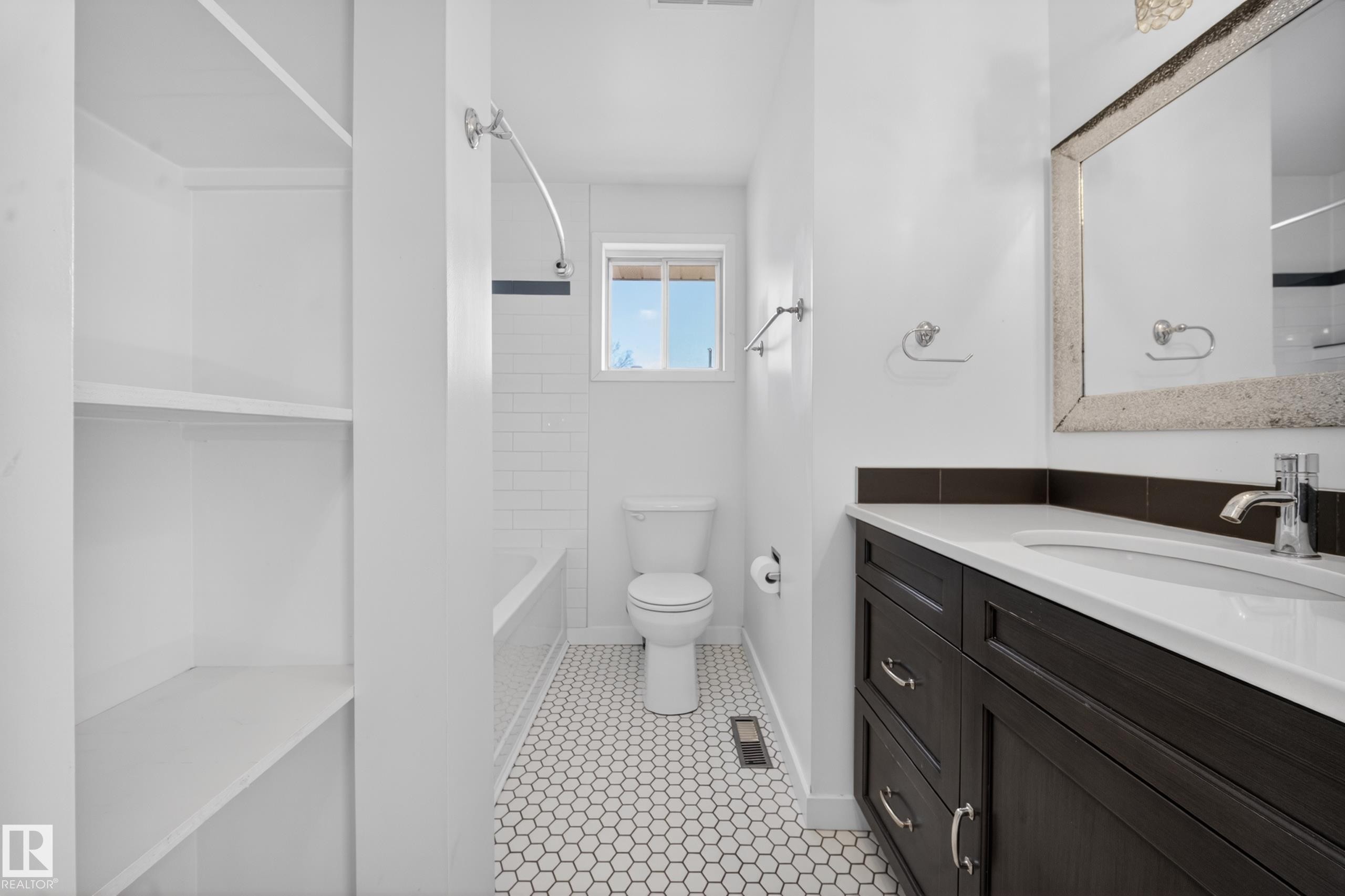 Bathroom featuring a dark wood-finish vanity with a white countertop and undermount sink, hexagonal tile flooring, built-in shelving, a full bath with subway tile surround, and a mirror with a decorative frame - 1767 61 Street, Edmonton, AB - Indoor Photo Showing Bathroom