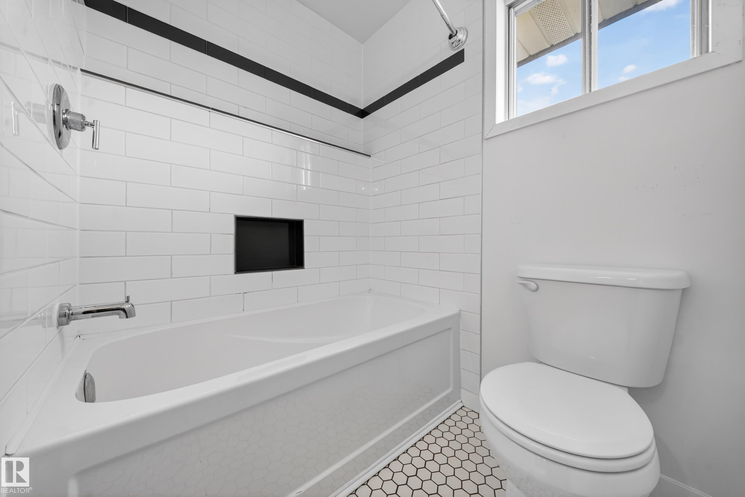 White subway tile tub surround with an integrated black accent niche, chrome fixtures, and a white bathtub - 1767 61 Street, Edmonton, AB - Indoor Photo Showing Bathroom