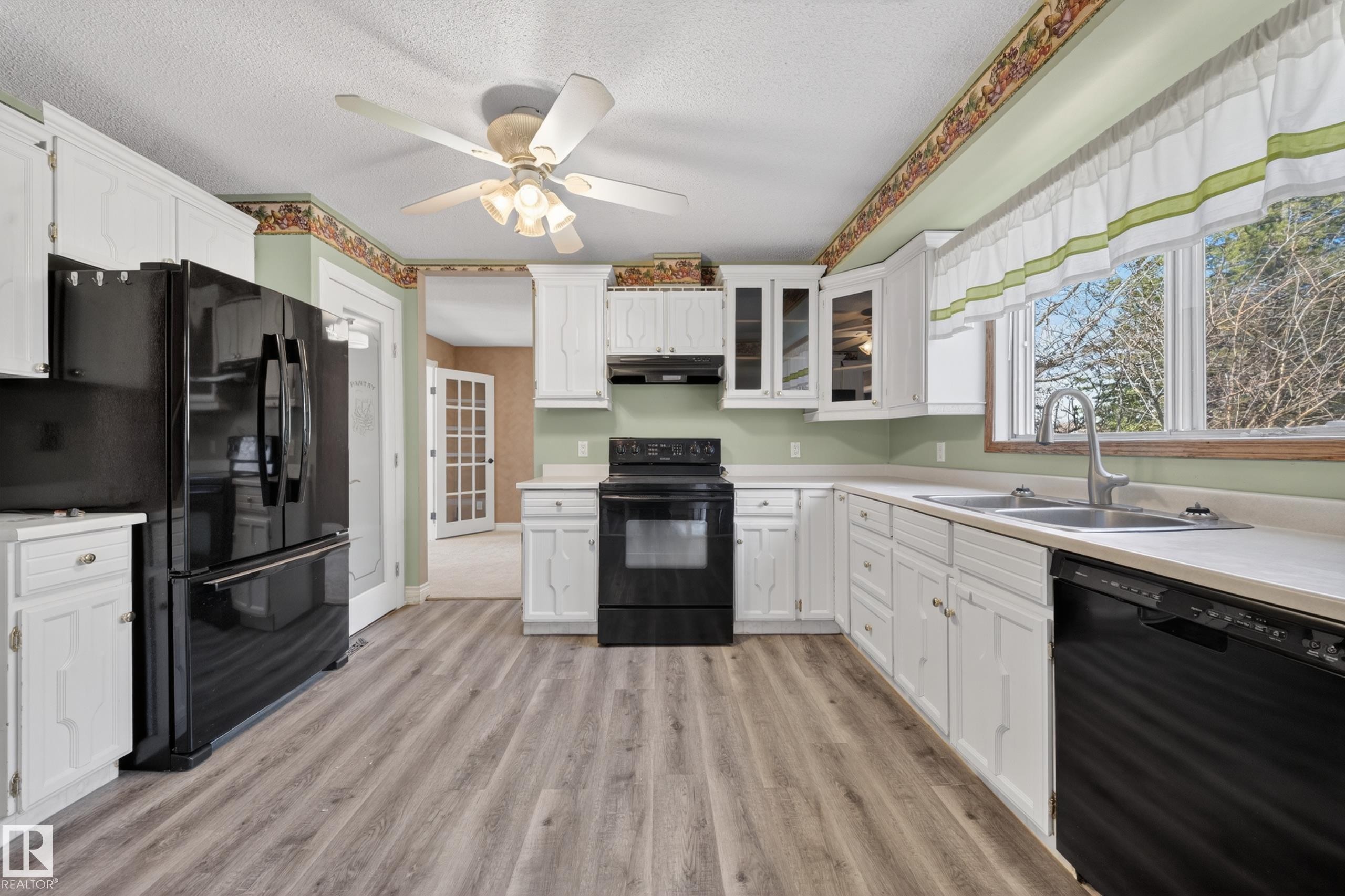 Kitchen featuring wood-finish flooring, white cabinetry, black appliances, and a double basin sink with a gooseneck faucet - 1767 61 Street, Edmonton, AB - Indoor Photo Showing Kitchen With Double Sink