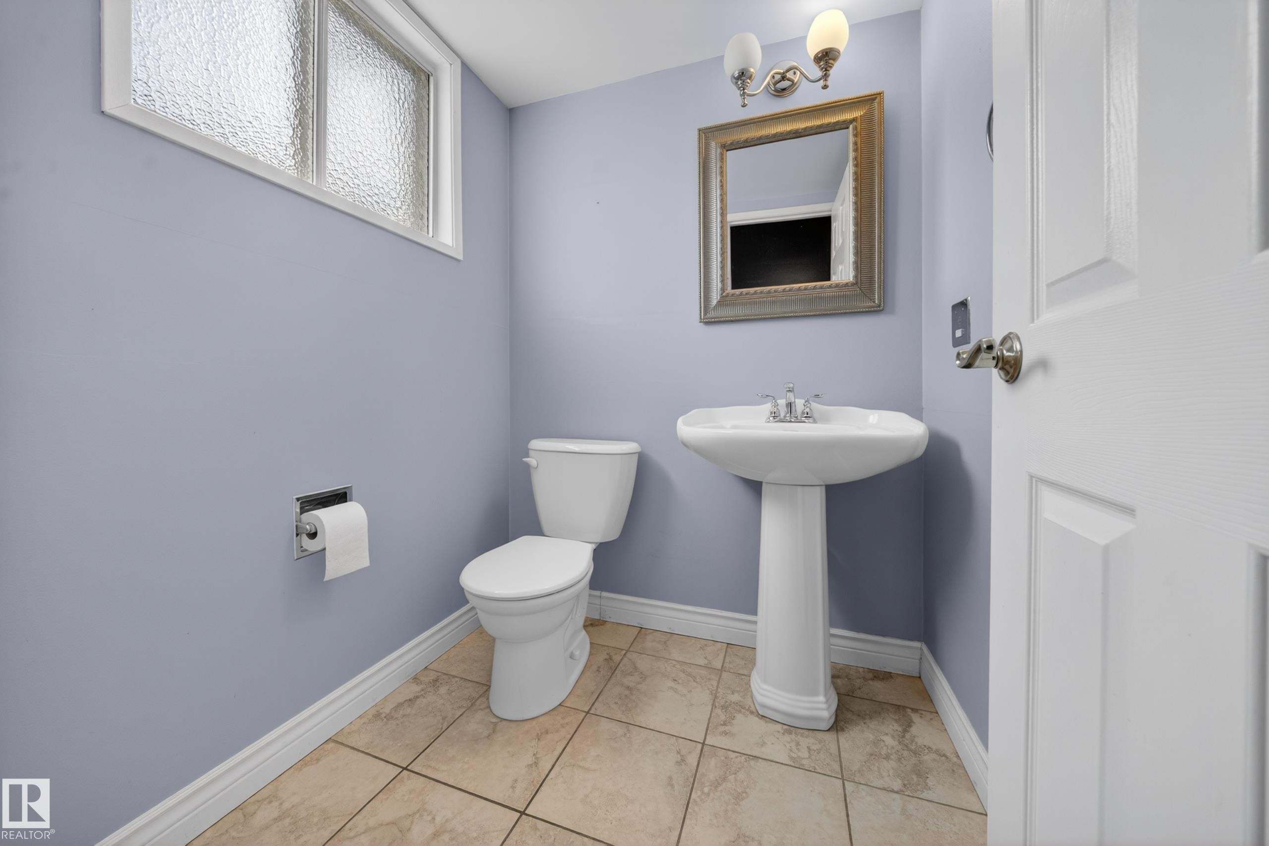 Bathroom featuring a pedestal sink, white toilet, tiled flooring, framed wall mirror, and a wall-mounted light fixture - 1767 61 Street, Edmonton, AB - Indoor Photo Showing Bathroom