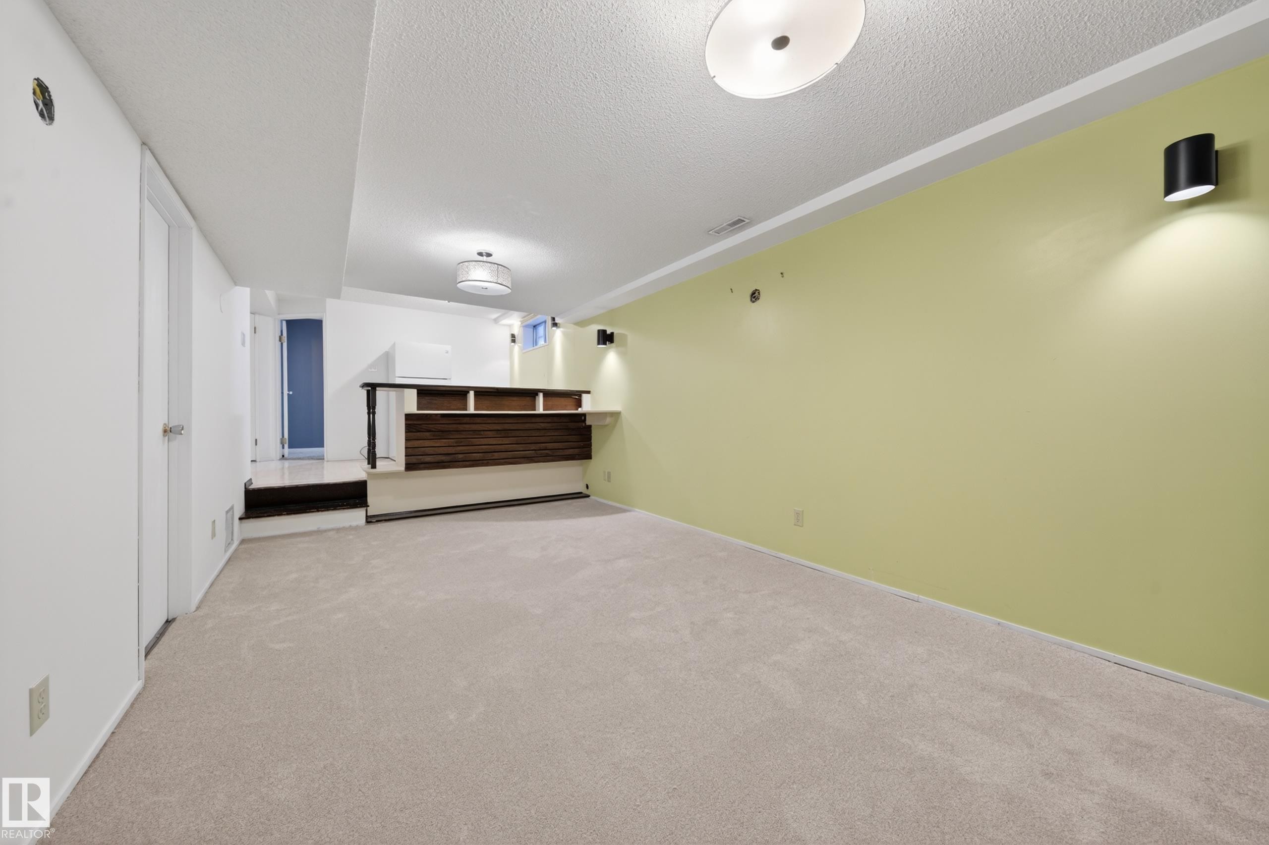 Spacious recreation room featuring light-colored carpeting, a built-in wet bar with dark wood-finish paneling, and a light green accent wall - 1767 61 Street, Edmonton, AB - Indoor Photo Showing Other Room