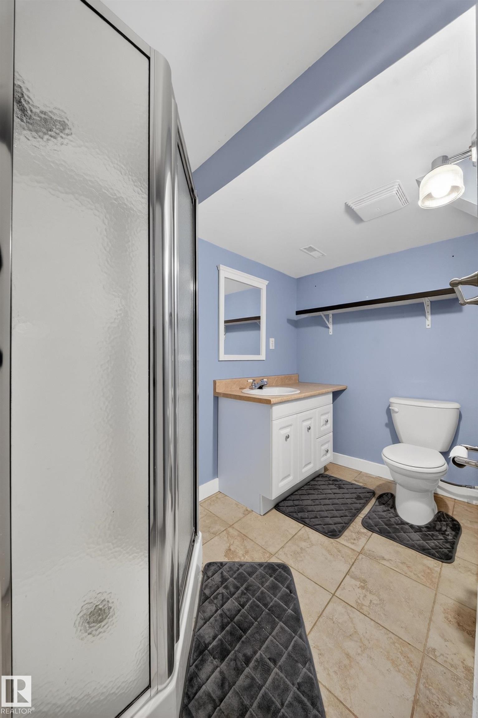 Bathroom featuring a shower enclosure with textured glass, a white vanity with a light wood-finish countertop, a single basin sink, and tile flooring - 1767 61 Street, Edmonton, AB - Indoor Photo Showing Bathroom