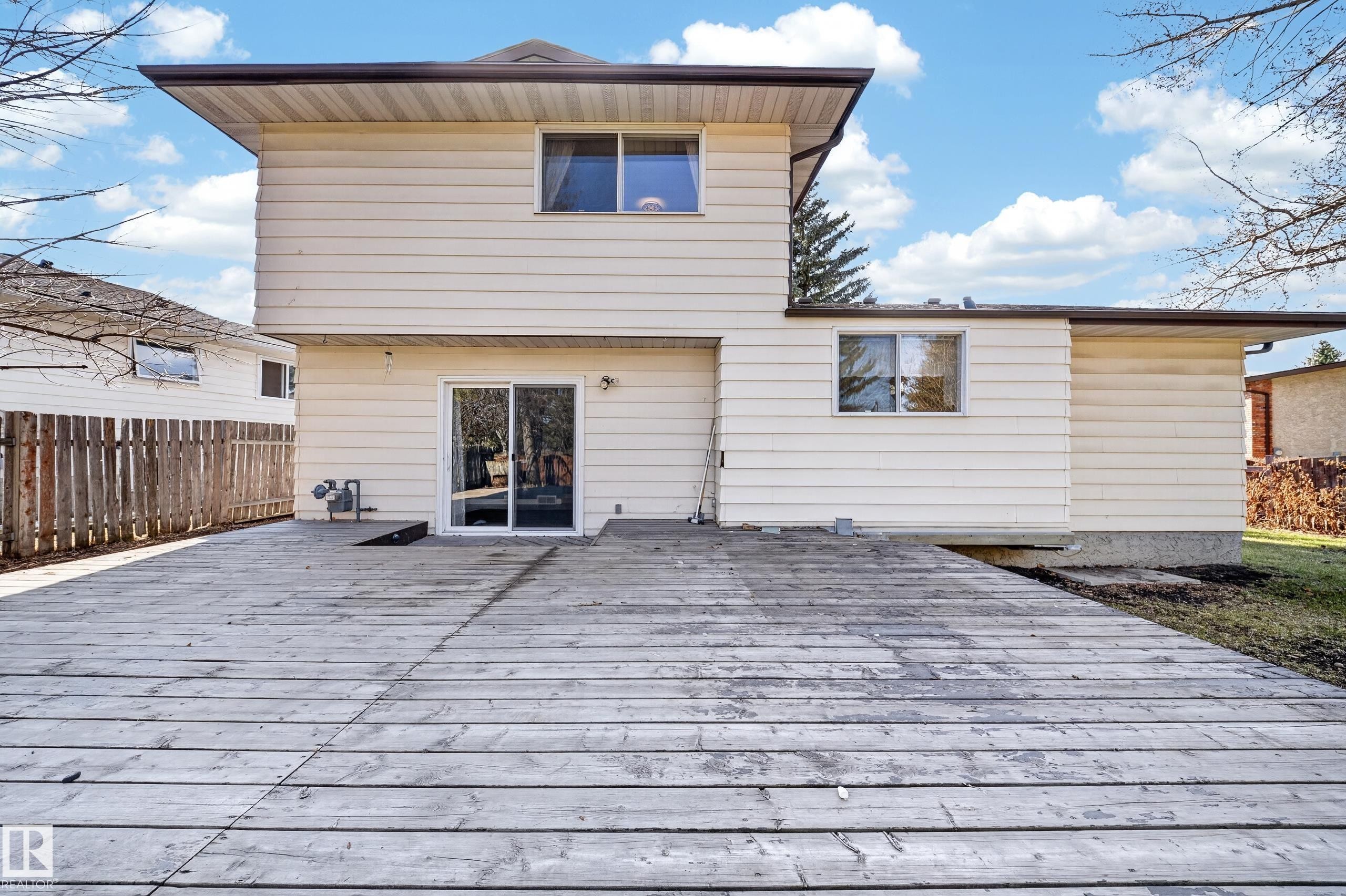 Expansive wood deck with a ground-level entrance, featuring a sliding glass door and multiple windows on the rear facade - 1767 61 Street, Edmonton, AB - Outdoor With Exterior