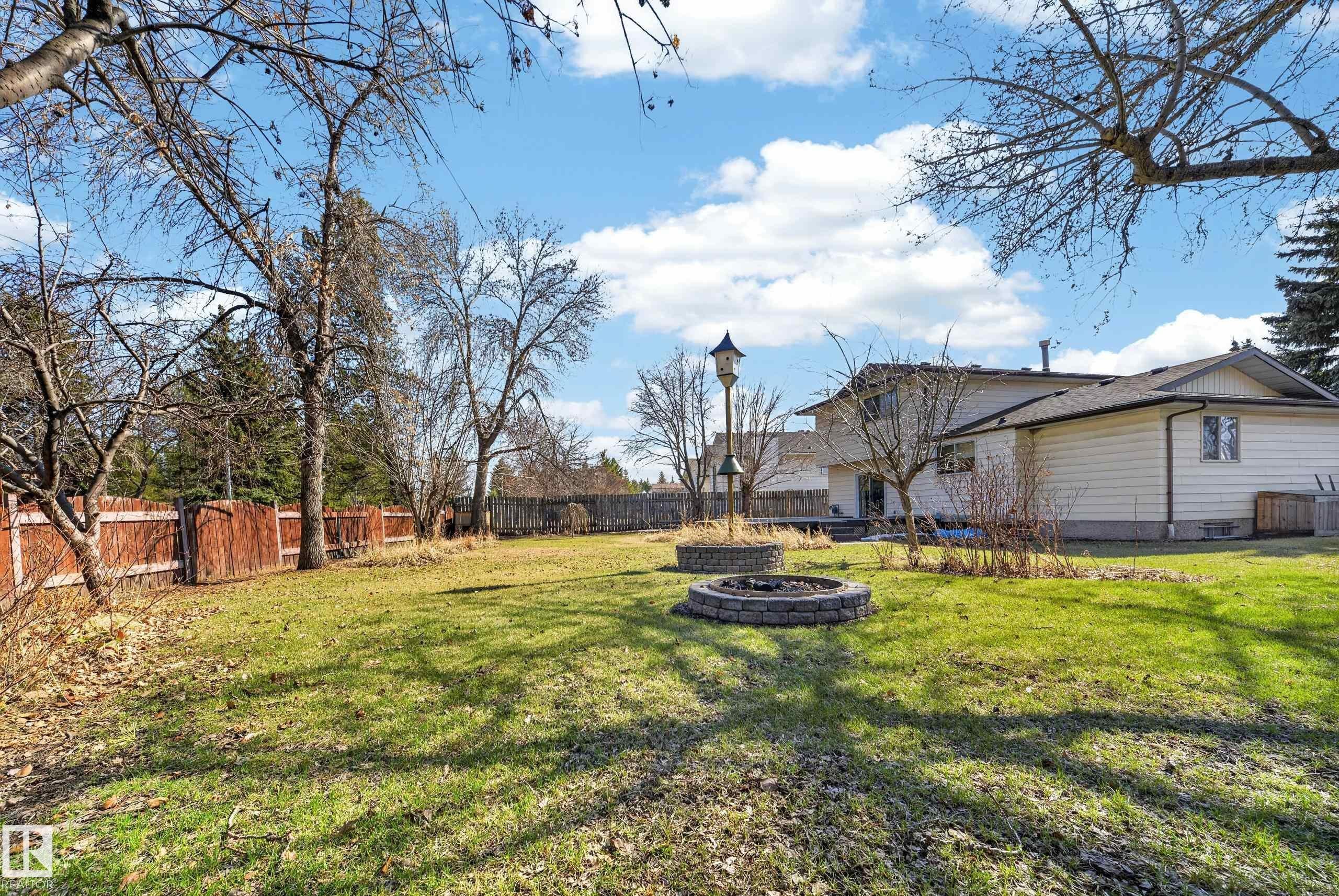 Expansive rear yard featuring a manicured lawn, two stone-clad fire pits, a tall birdhouse structure, a wood privacy fence, and mature trees - 1767 61 Street, Edmonton, AB - Outdoor