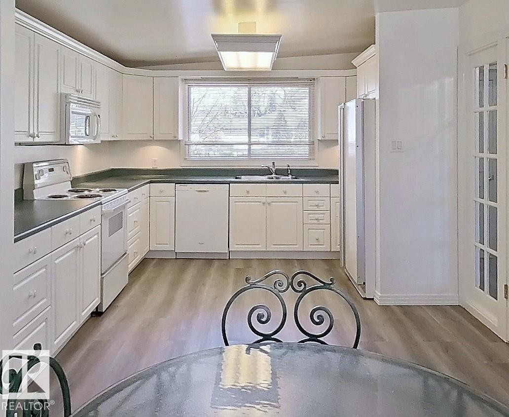 Kitchen featuring white cabinetry, dark countertops, built-in microwave, white range, and wood-finish flooring - 9624 75 Street, Edmonton, AB - Indoor Photo Showing Kitchen With Double Sink