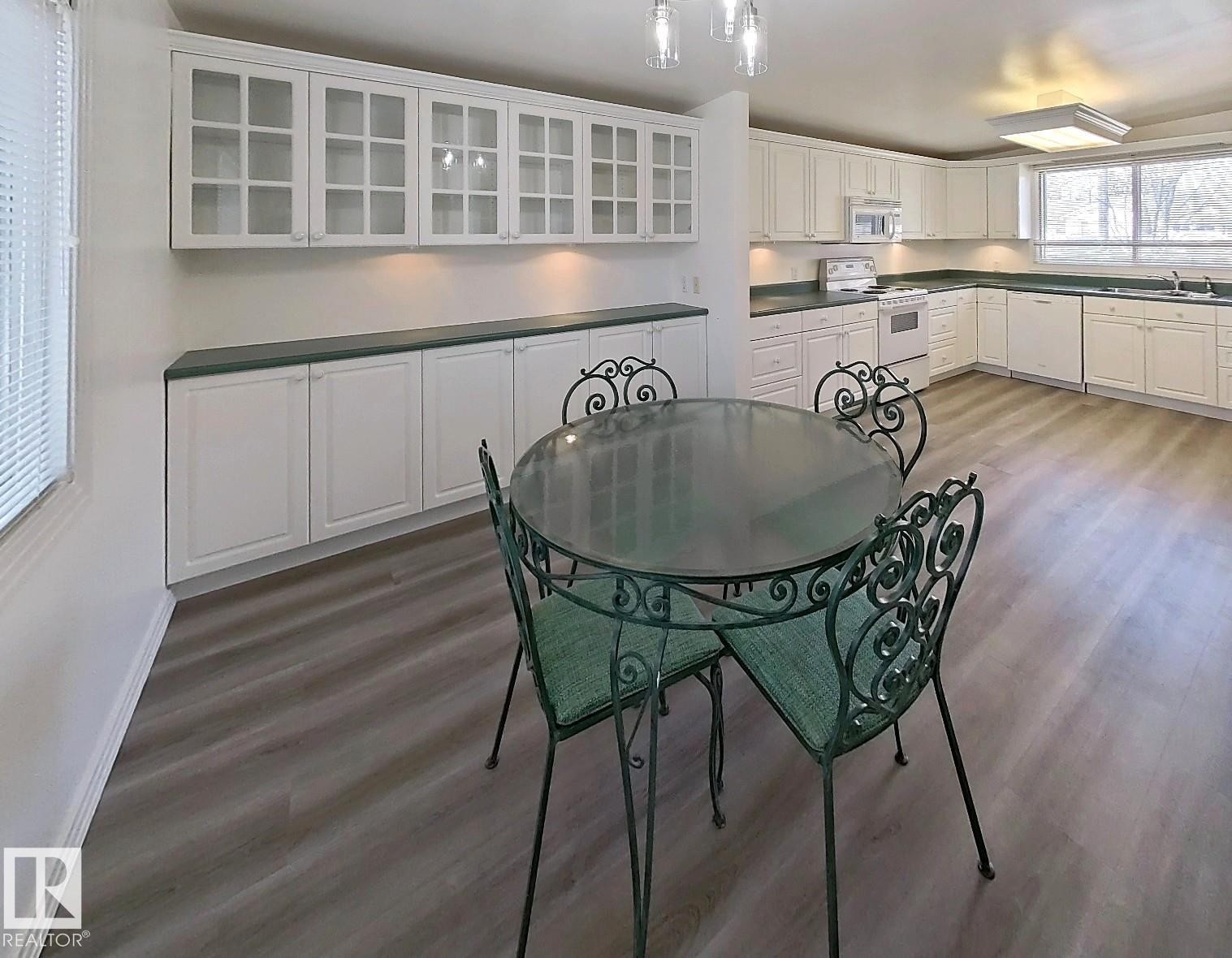 Spacious kitchen featuring extensive white cabinetry, dark green countertops, wood-finish flooring, and a large window - 9624 75 Street, Edmonton, AB - Indoor