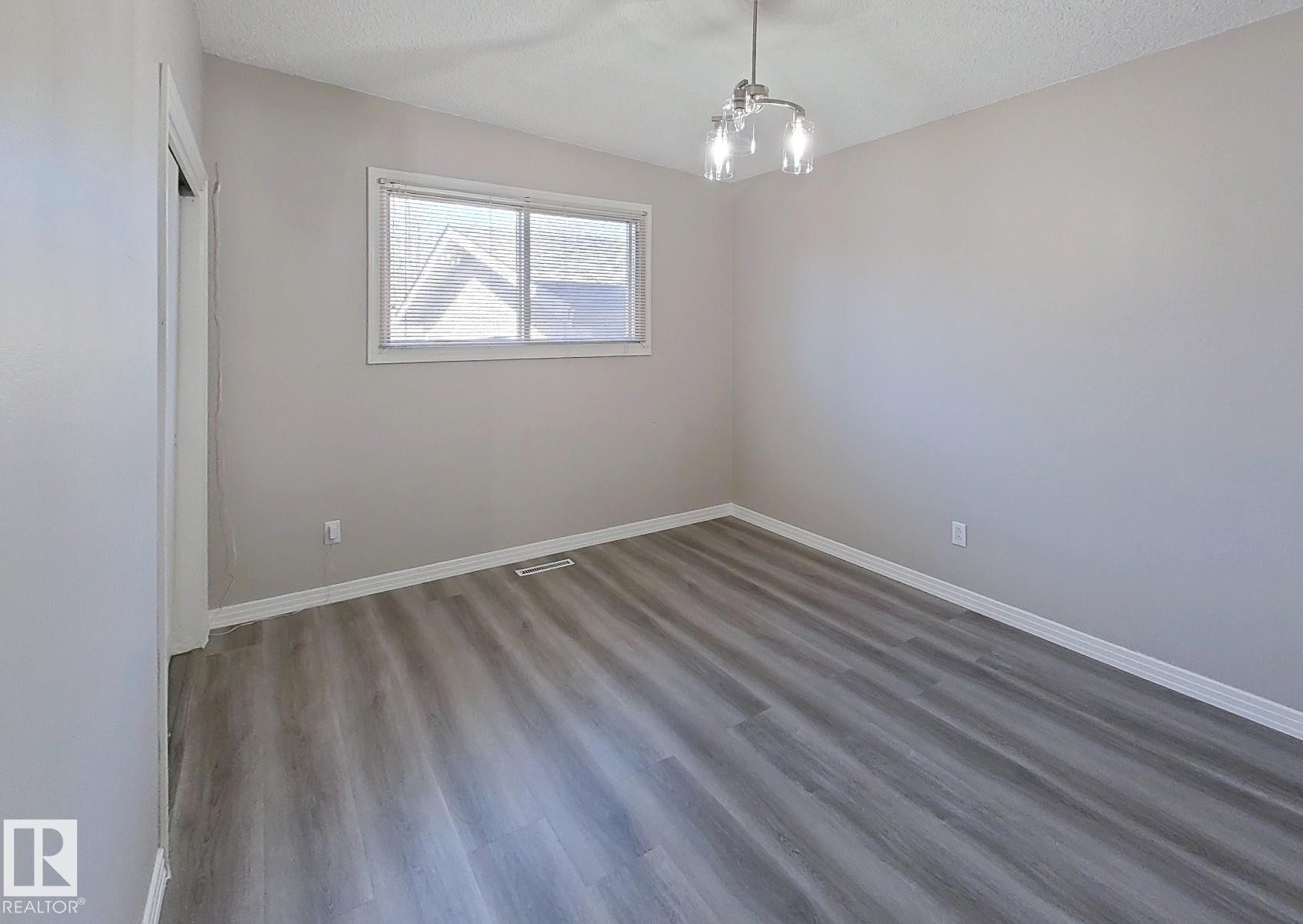 Room featuring wood-finish flooring, neutral wall paint, white trim, and a window with white casing - 9624 75 Street, Edmonton, AB - Indoor Photo Showing Other Room