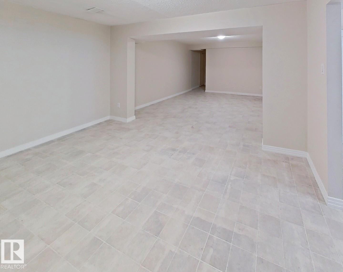 Spacious room featuring light-toned tiled flooring, neutral wall paint, and white baseboards - 9624 75 Street, Edmonton, AB - Indoor Photo Showing Other Room