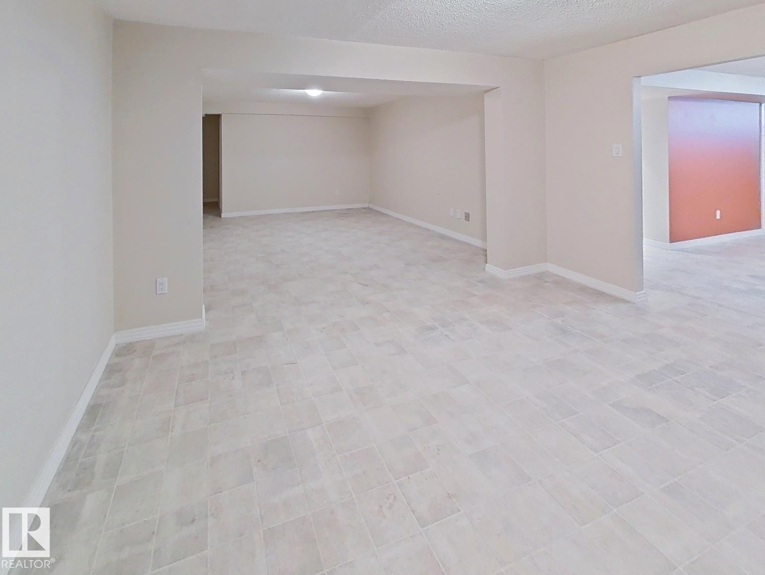 Spacious interior area featuring light-toned square-tile flooring, neutral wall paint, and white baseboards - 9624 75 Street, Edmonton, AB - Indoor Photo Showing Other Room