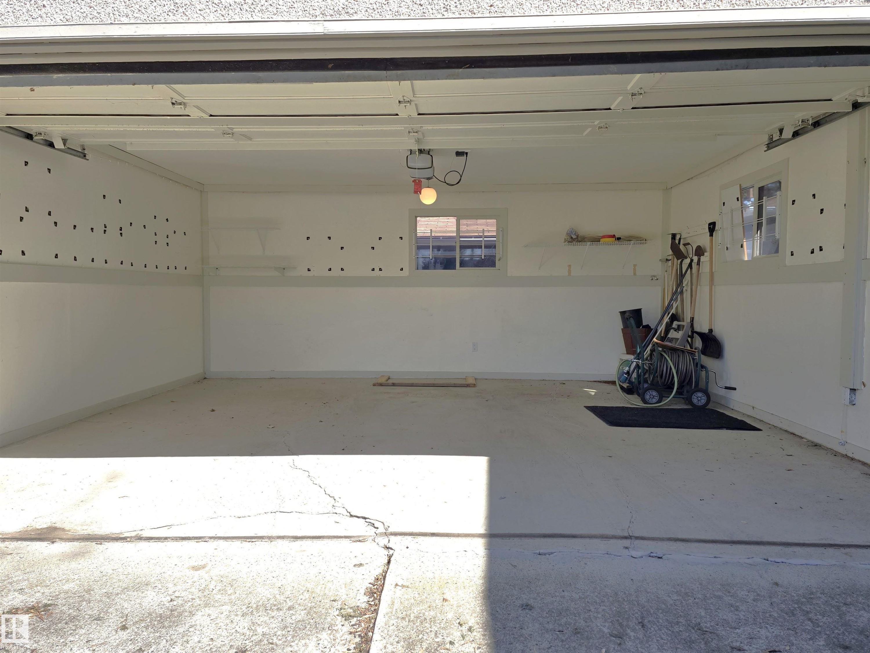 Spacious garage interior featuring concrete flooring, white painted walls, and built-in shelving - 9624 75 Street, Edmonton, AB - Indoor Photo Showing Garage