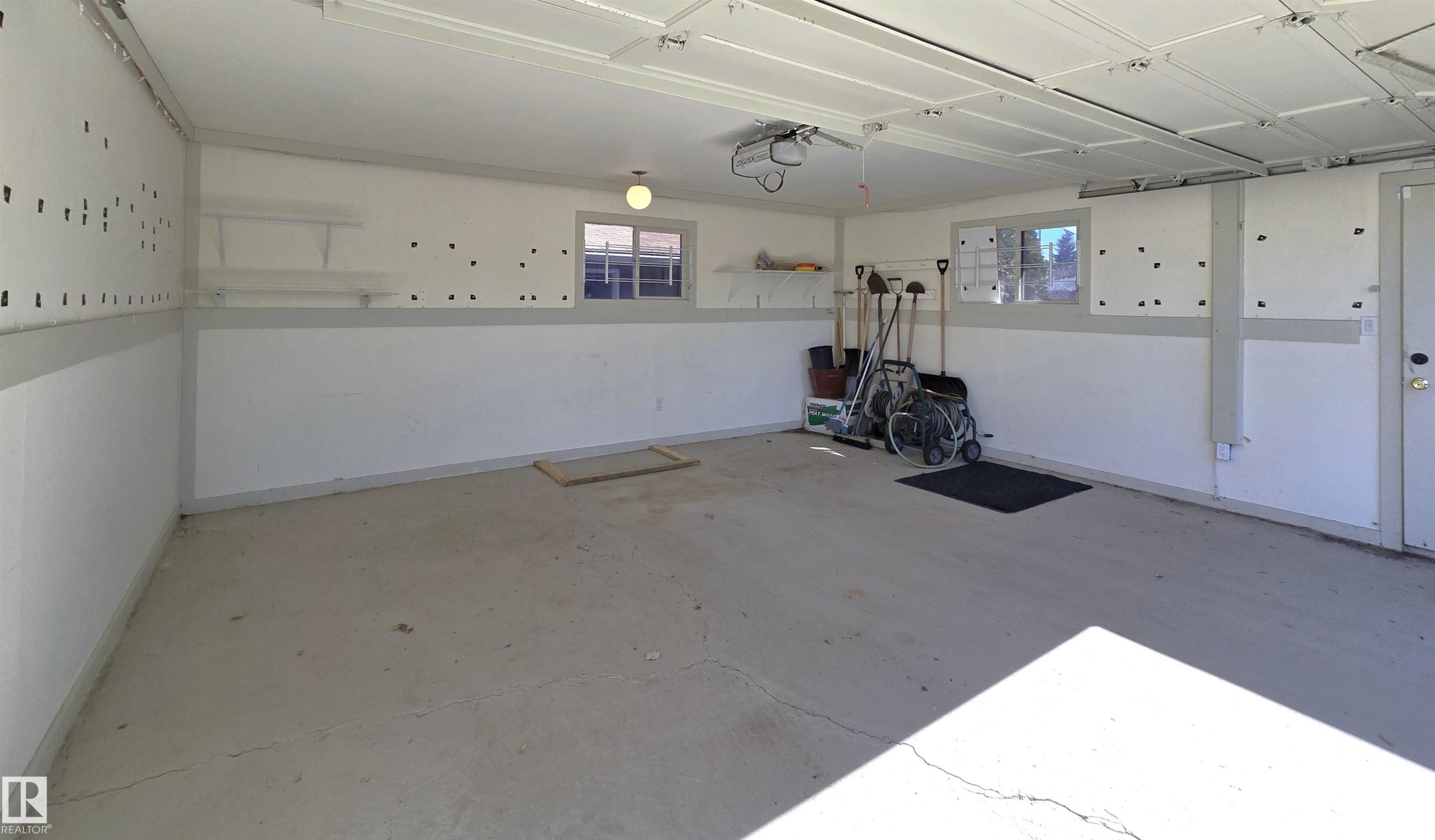 Spacious garage featuring a concrete floor, painted white walls with a gray wainscoting, and windows providing natural light - 9624 75 Street, Edmonton, AB - Indoor Photo Showing Garage