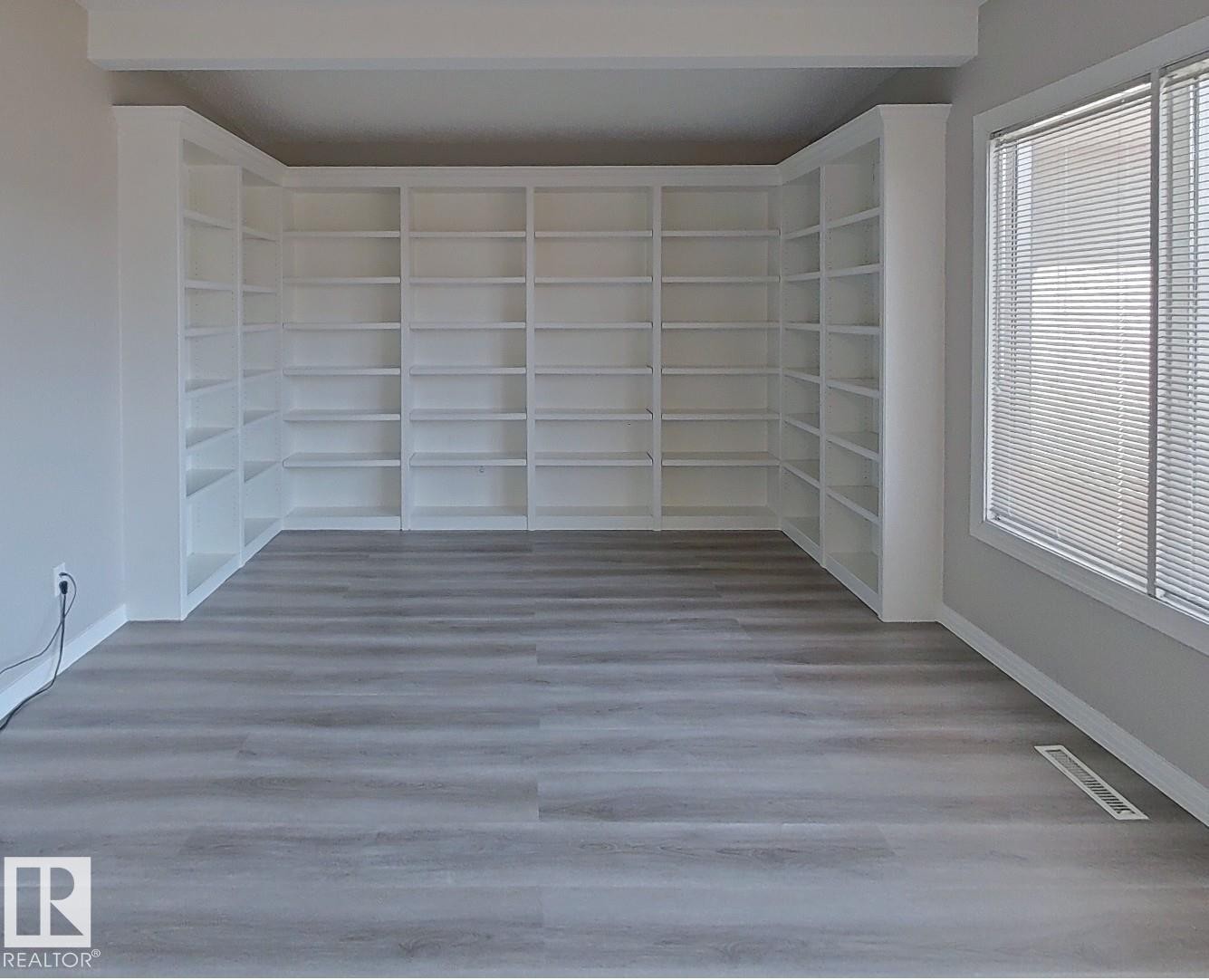 Room featuring extensive built-in white shelving, wood-finish flooring, and a large window with horizontal blinds - 9624 75 Street, Edmonton, AB - Indoor Photo Showing Other Room