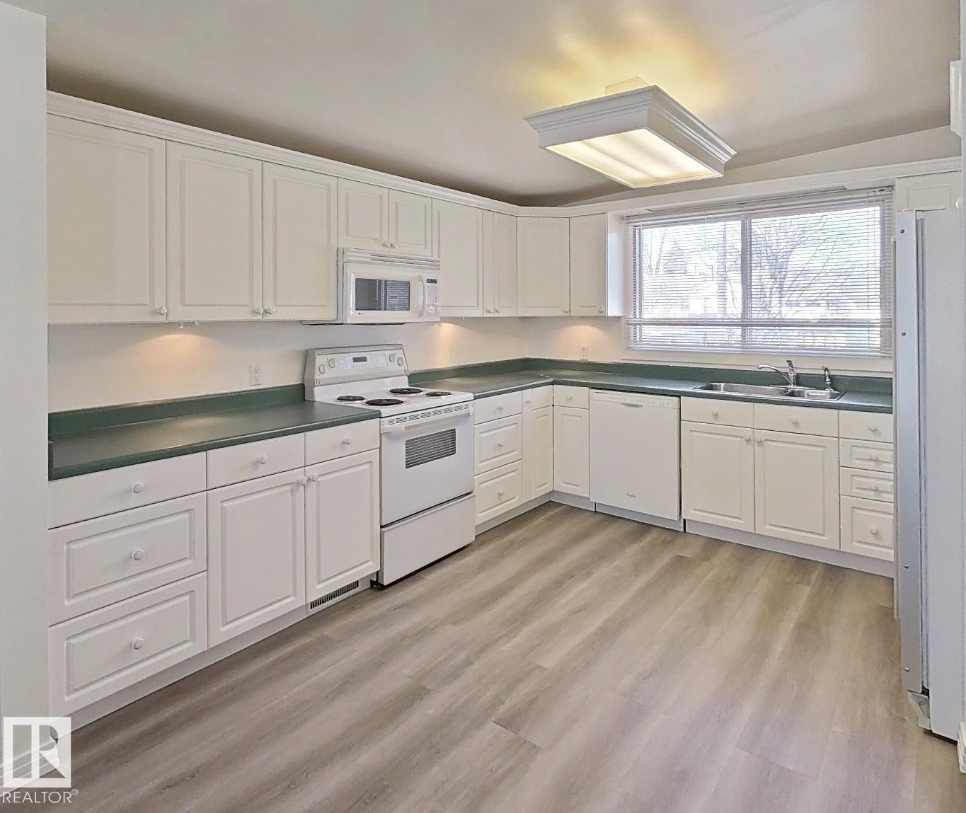Kitchen featuring white cabinetry, dark green countertops, a white electric range, a built-in microwave, and wood-finish flooring - 9624 75 Street, Edmonton, AB - Indoor Photo Showing Kitchen With Double Sink