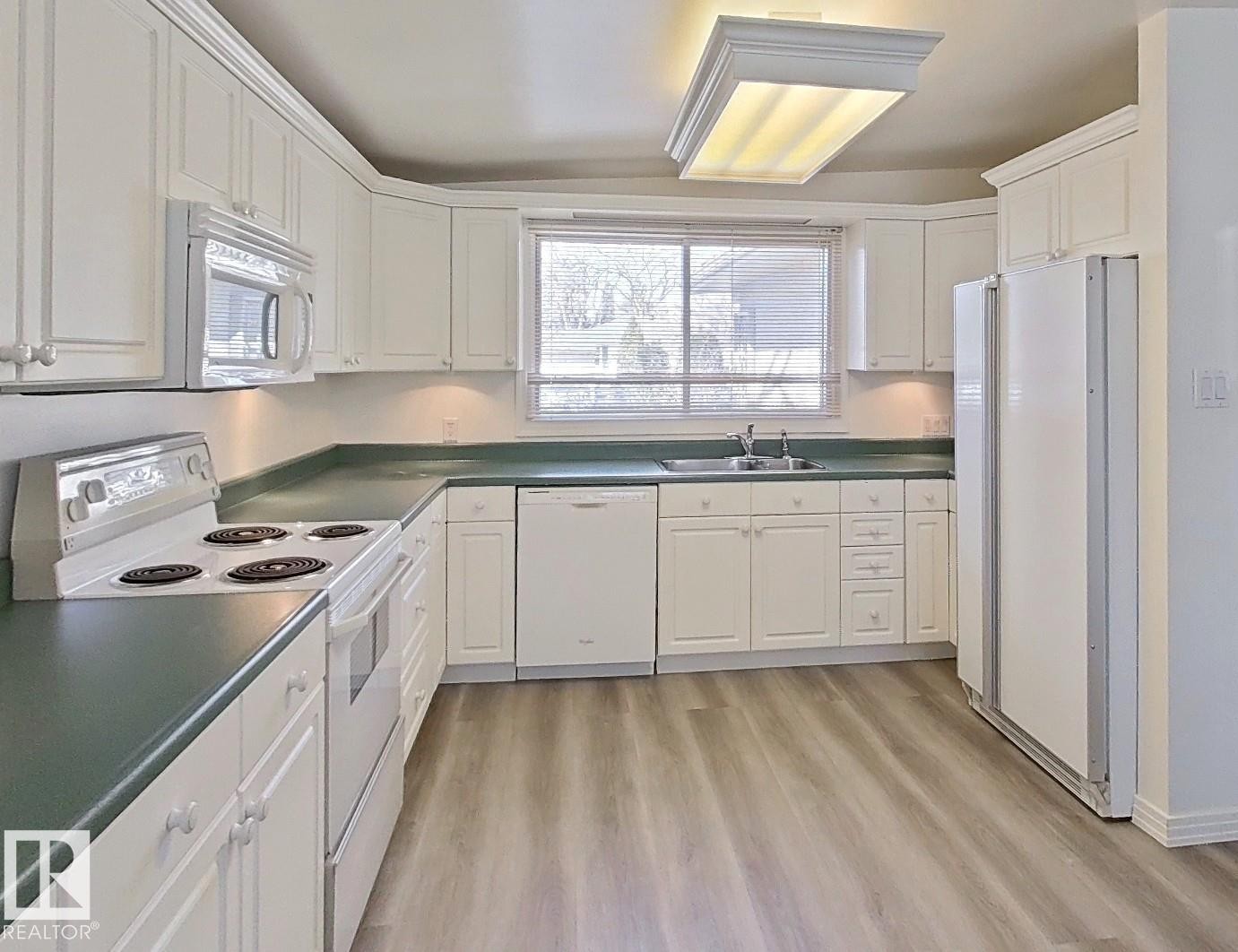 Kitchen featuring white cabinetry, green countertops, wood-finish flooring, and white appliances including a refrigerator, range, microwave, and dishwasher - 9624 75 Street, Edmonton, AB - Indoor Photo Showing Kitchen With Double Sink