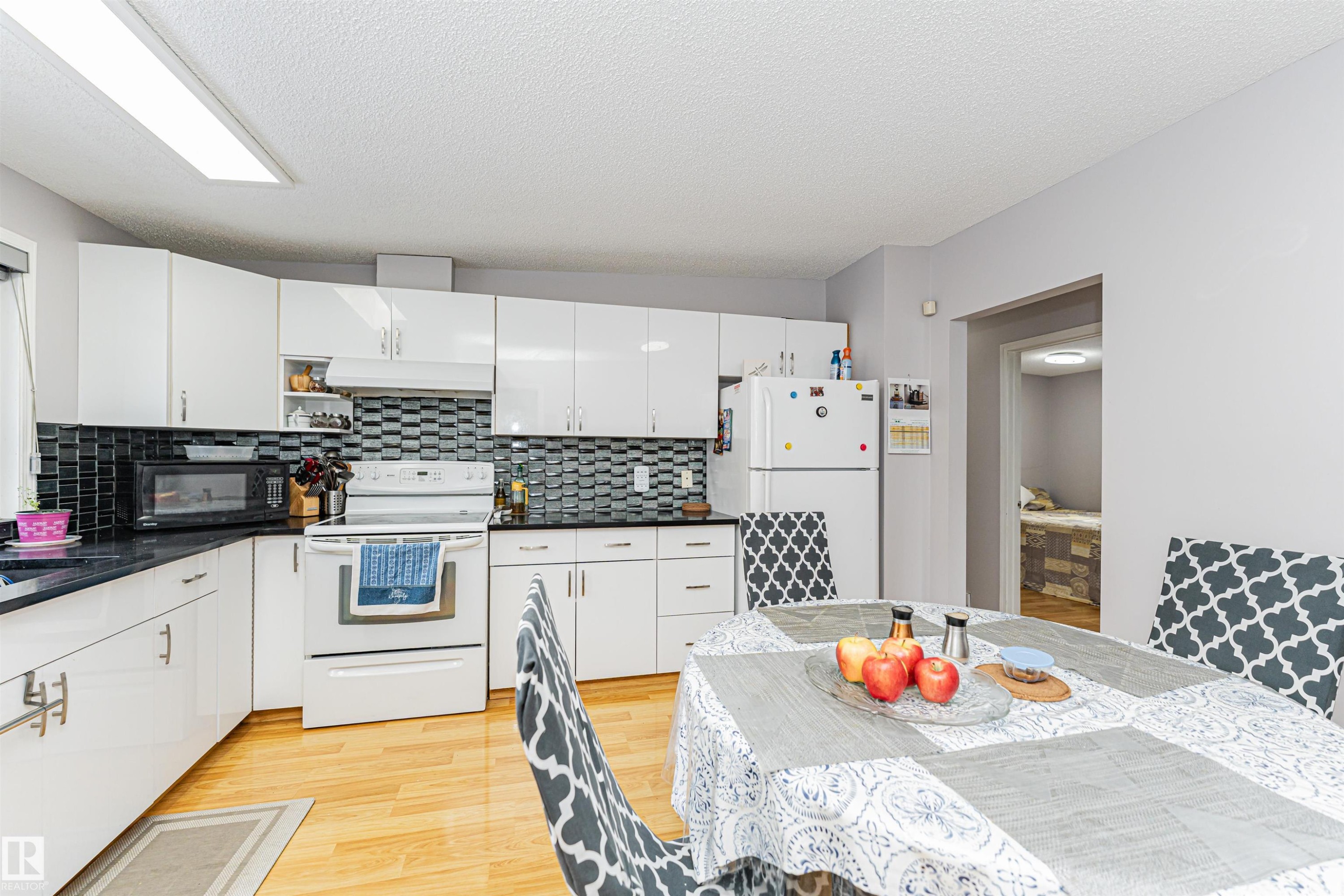 The kitchen features white cabinetry, dark countertops, a tiled backsplash, and hardwood flooring - 10412 39 Avenue, Edmonton, AB - Indoor Photo Showing Kitchen