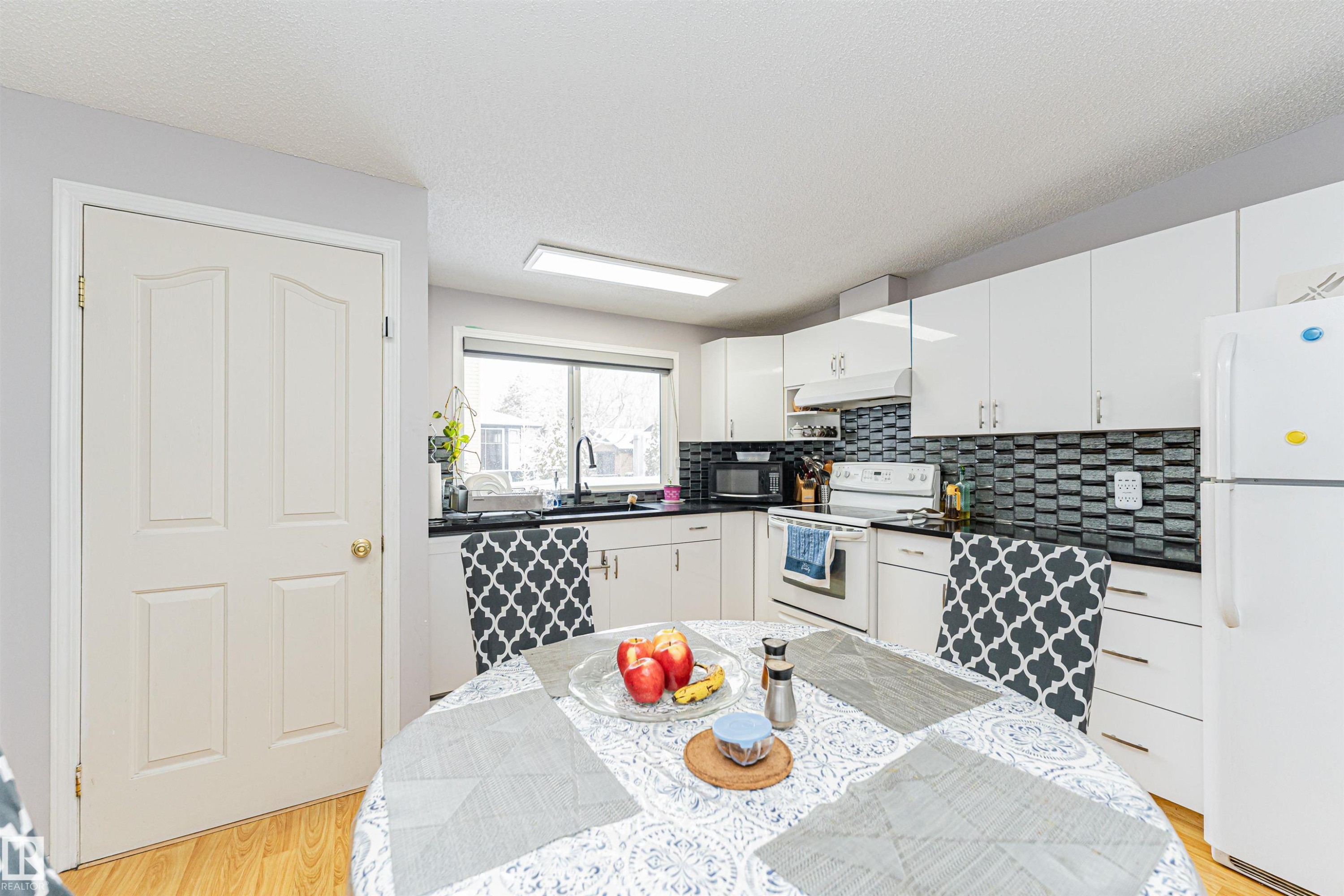 The kitchen features white cabinetry, a black and white tiled backsplash, and light wood flooring - 10412 39 Avenue, Edmonton, AB - Indoor Photo Showing Kitchen