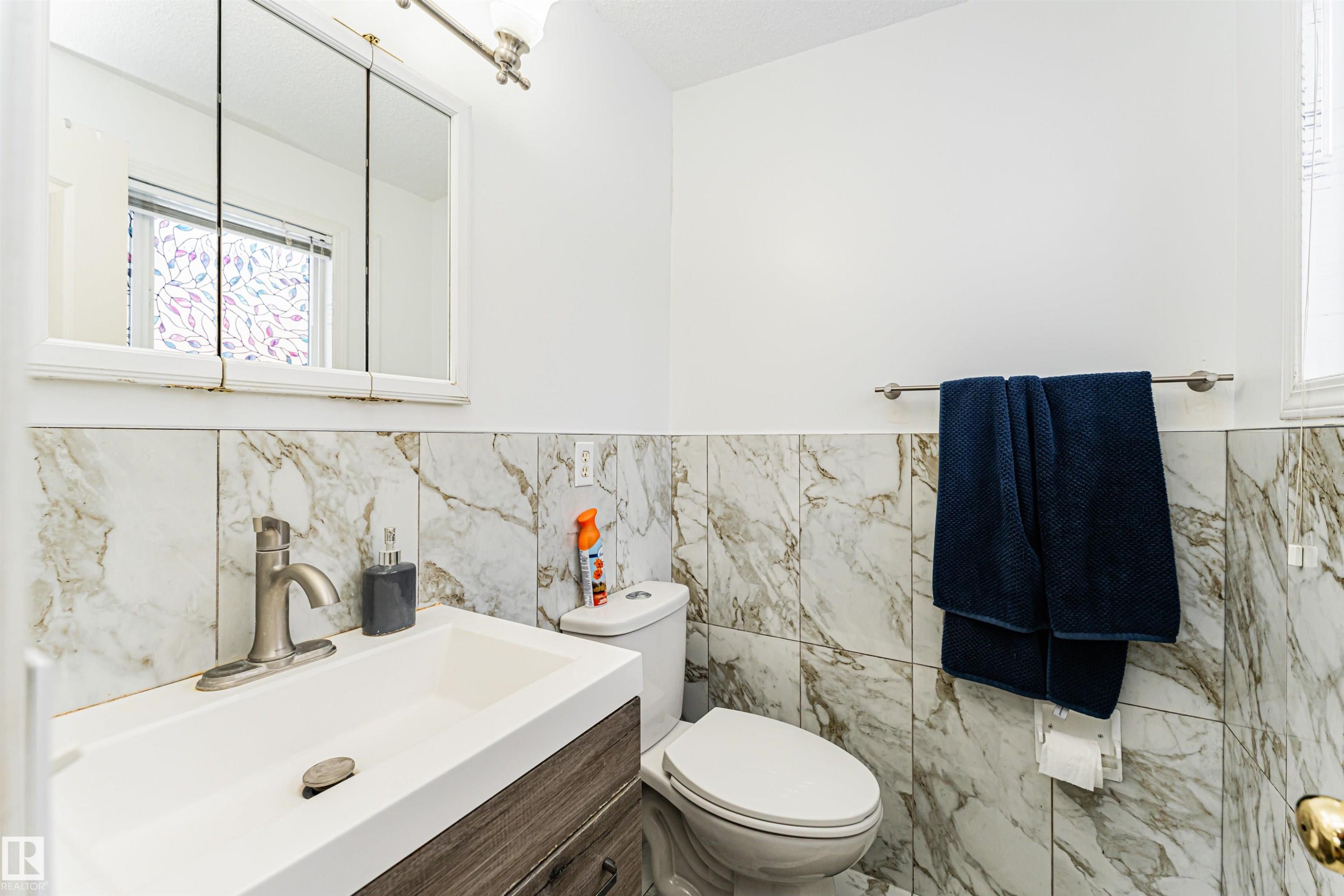 Bathroom with a modern vanity, white sink, and stone tile wainscoting - 10412 39 Avenue, Edmonton, AB - Indoor Photo Showing Bathroom