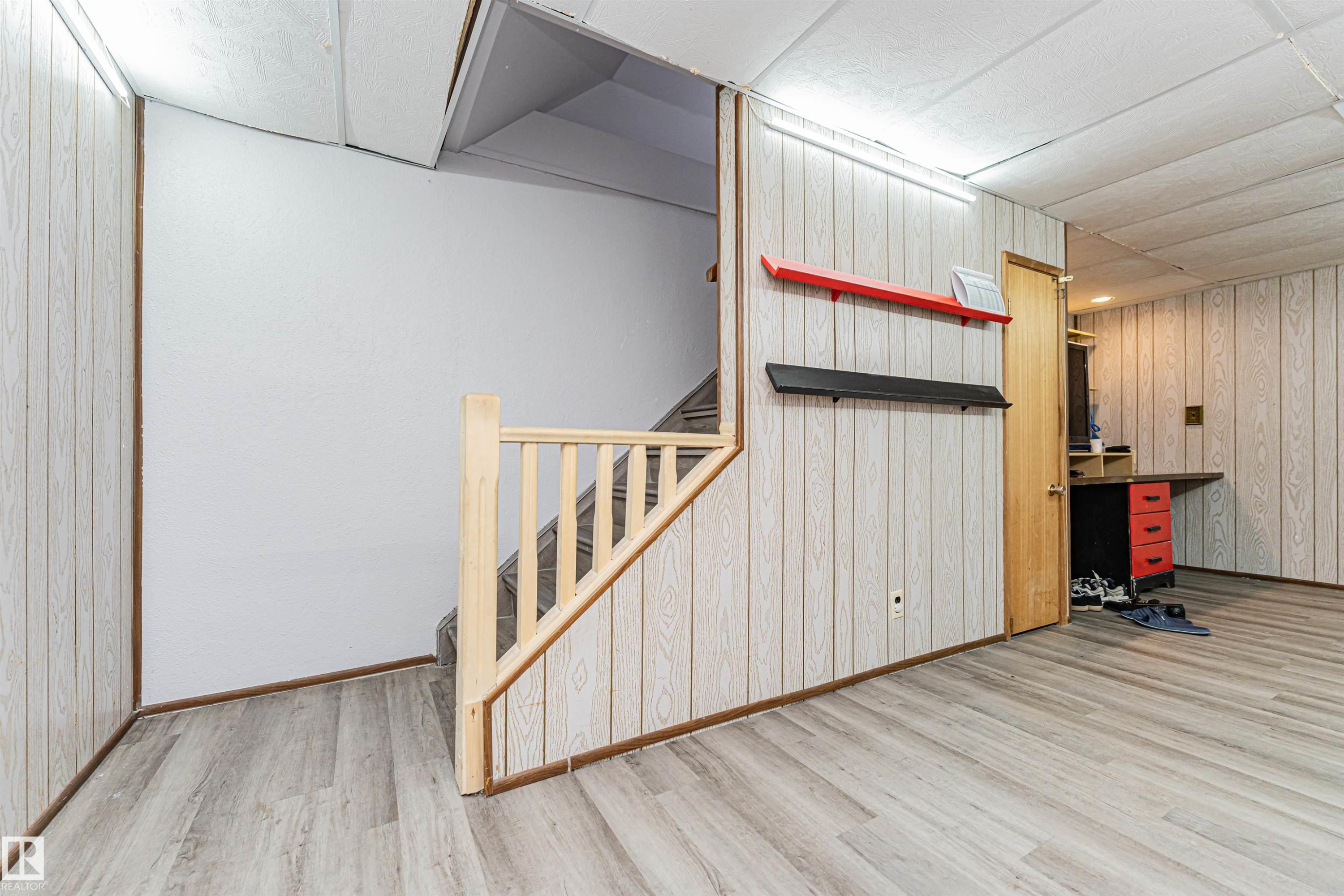 This space features light wood-look flooring, light-colored wall paneling, and a staircase with a wooden banister - 10412 39 Avenue, Edmonton, AB - Indoor Photo Showing Other Room