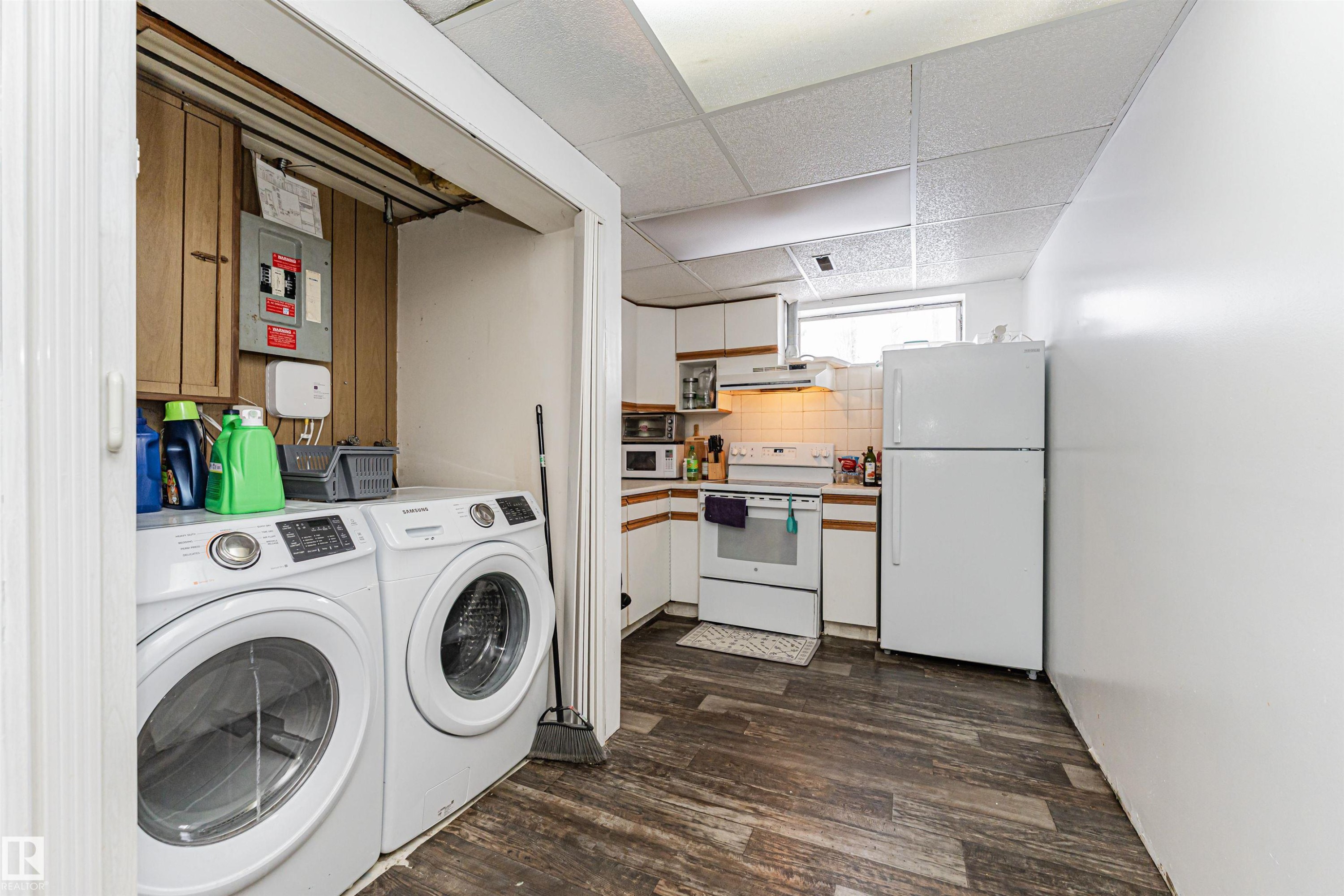 The property features a dedicated laundry area with white front-loading machines, and a kitchen area with white cabinetry, a window, and a white refrigerator - 10412 39 Avenue, Edmonton, AB - Indoor Photo Showing Laundry Room