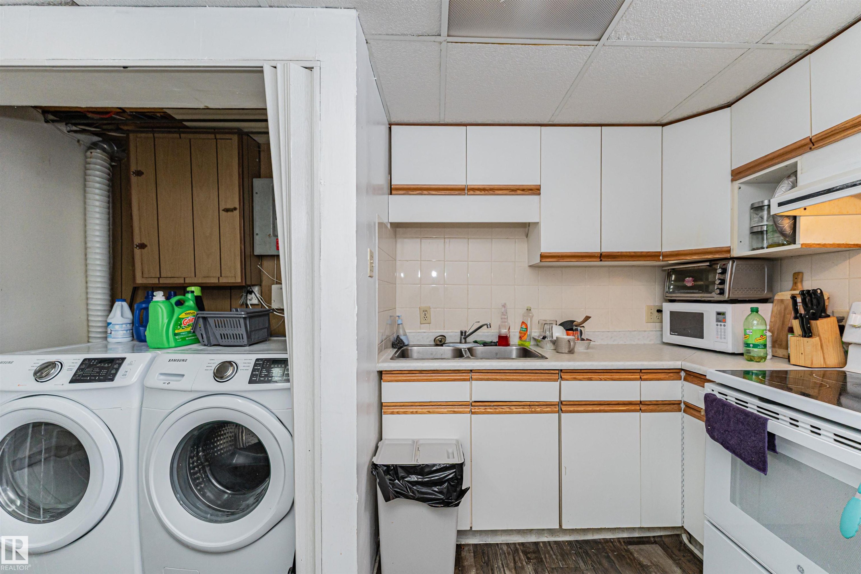 The kitchen features white cabinetry with wood trim, a double basin stainless steel sink, and a white tiled backsplash - 10412 39 Avenue, Edmonton, AB - Indoor Photo Showing Laundry Room