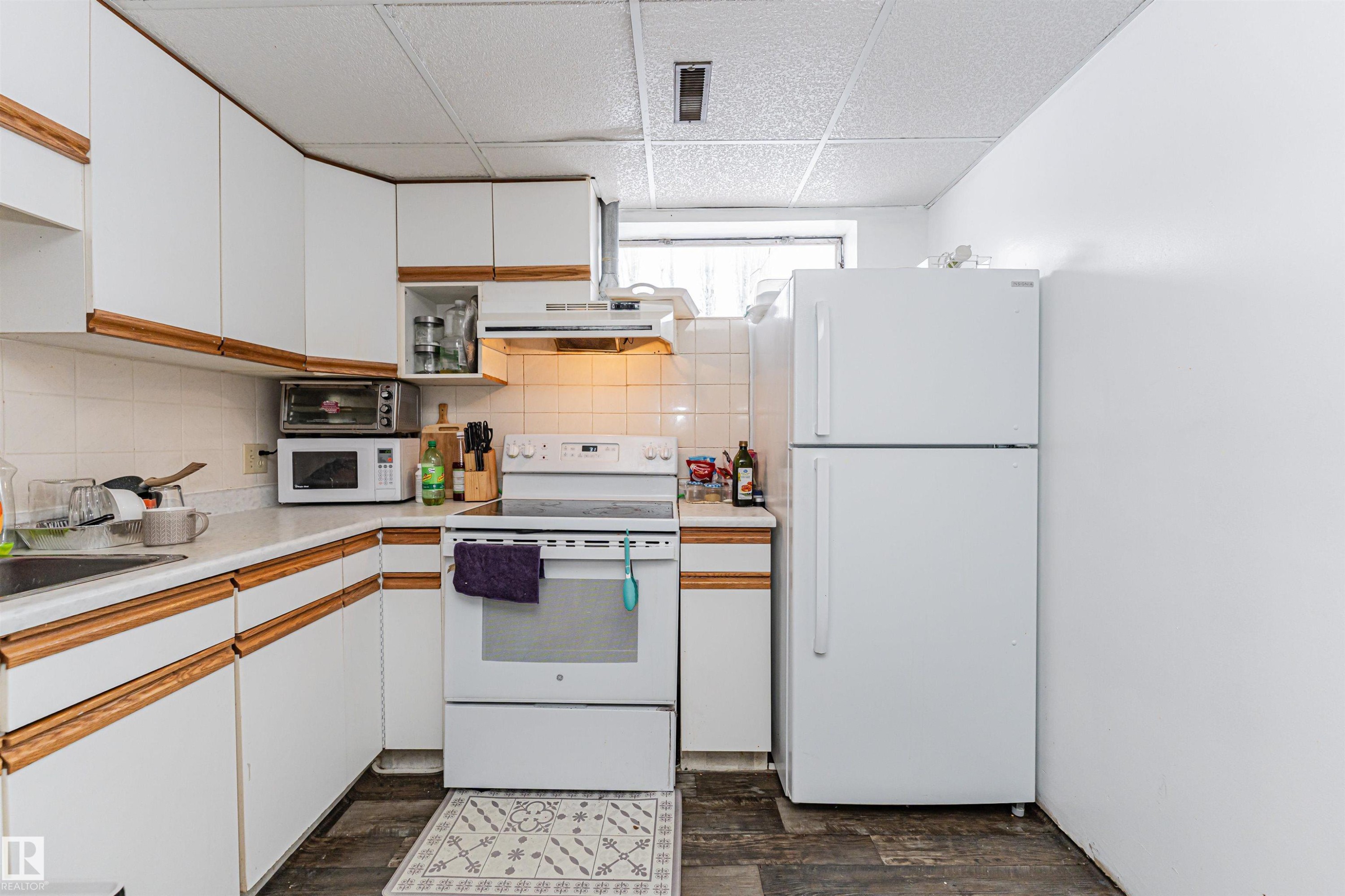 The kitchen features white cabinetry with wood trim, a white tile backsplash, and a white refrigerator - 10412 39 Avenue, Edmonton, AB - Indoor Photo Showing Kitchen