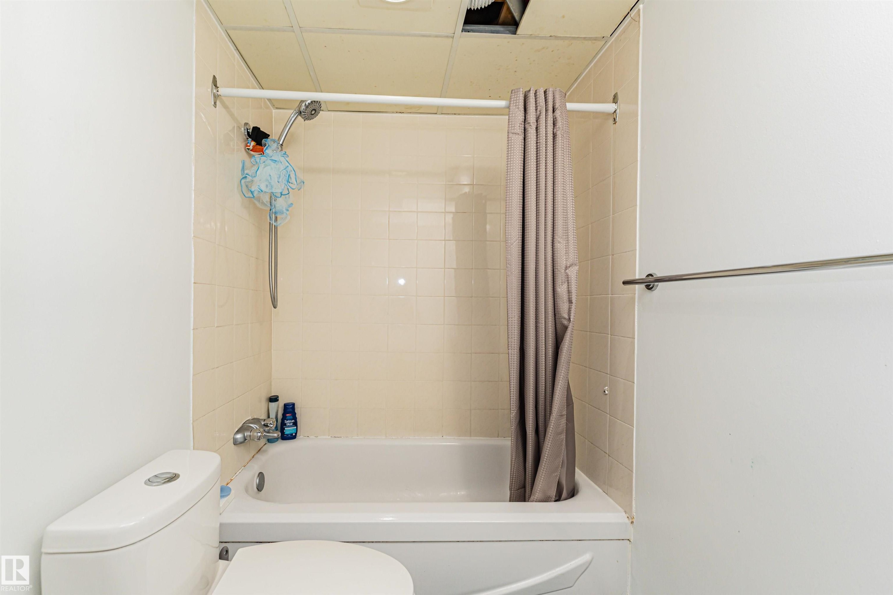 Bathroom featuring a bathtub with a shower and neutral-toned tiled surround - 10412 39 Avenue, Edmonton, AB - Indoor Photo Showing Bathroom