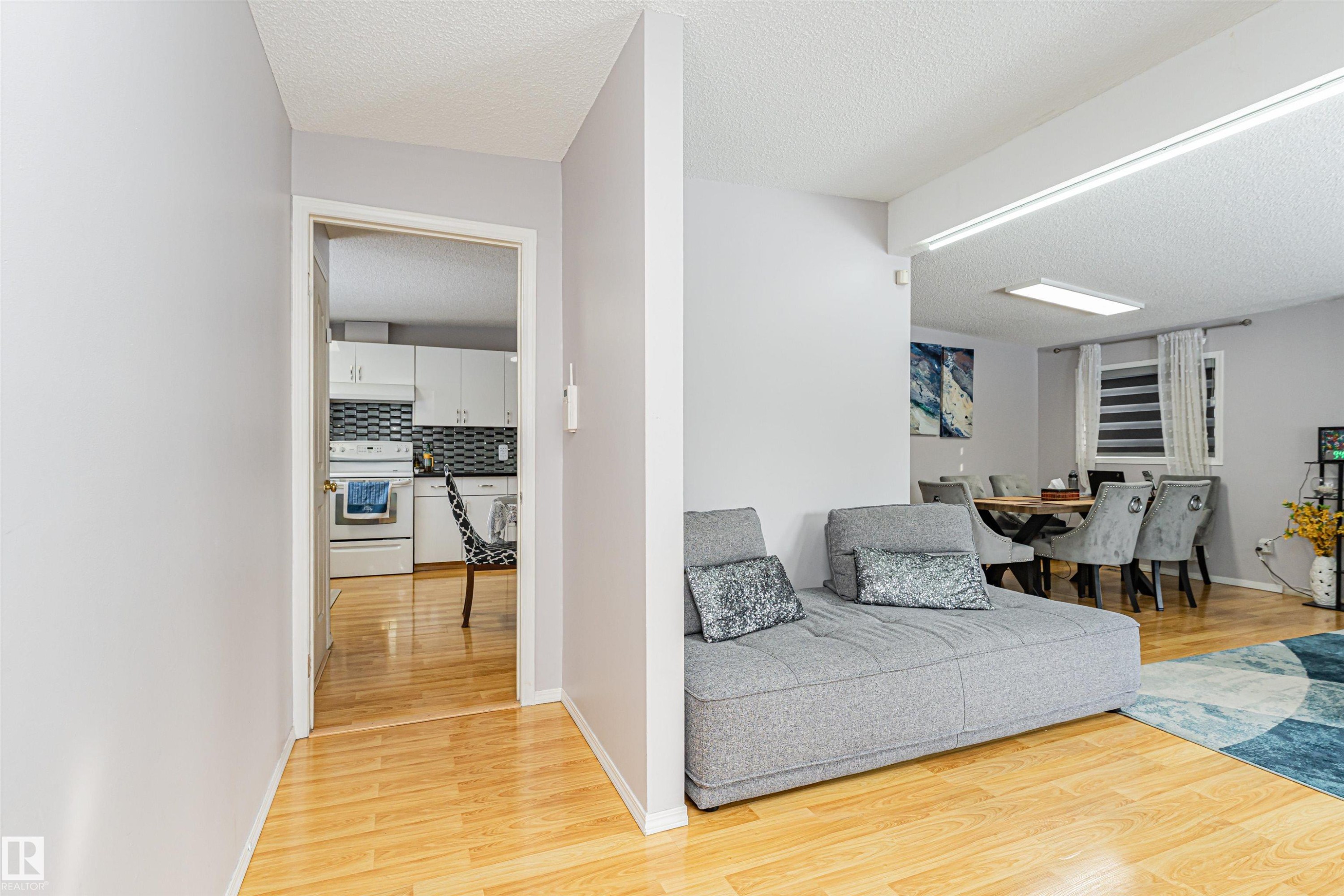 The property features light-colored wood flooring in the foreground, with a doorway leading into a kitchen area - 10412 39 Avenue, Edmonton, AB - Indoor Photo Showing Other Room