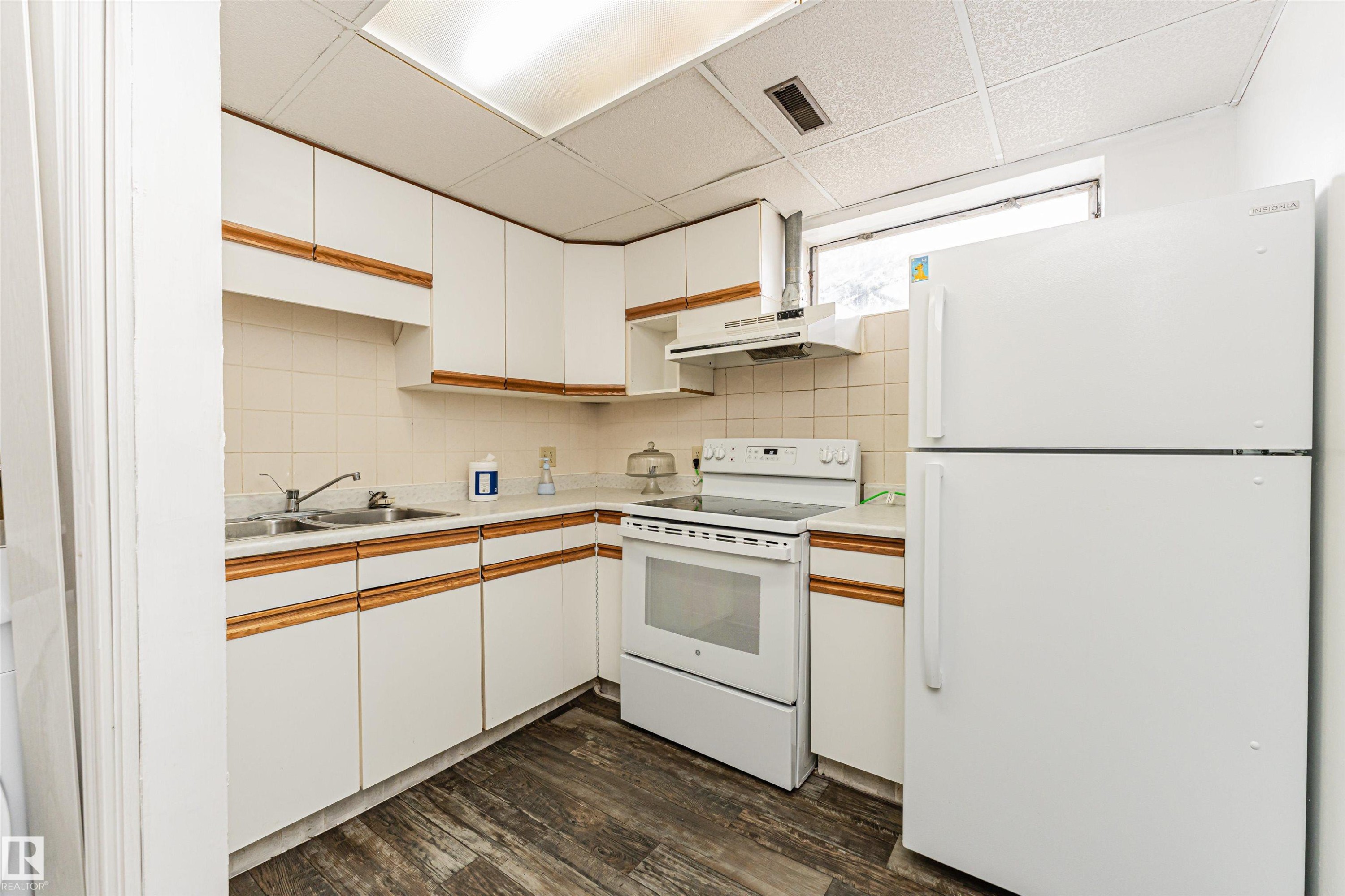 Kitchen featuring white cabinetry with wood-finish accents, a double basin stainless steel sink, a white electric range, a white refrigerator, and wood-finish flooring - 10412 39 Avenue, Edmonton, AB - Indoor Photo Showing Kitchen With Double Sink