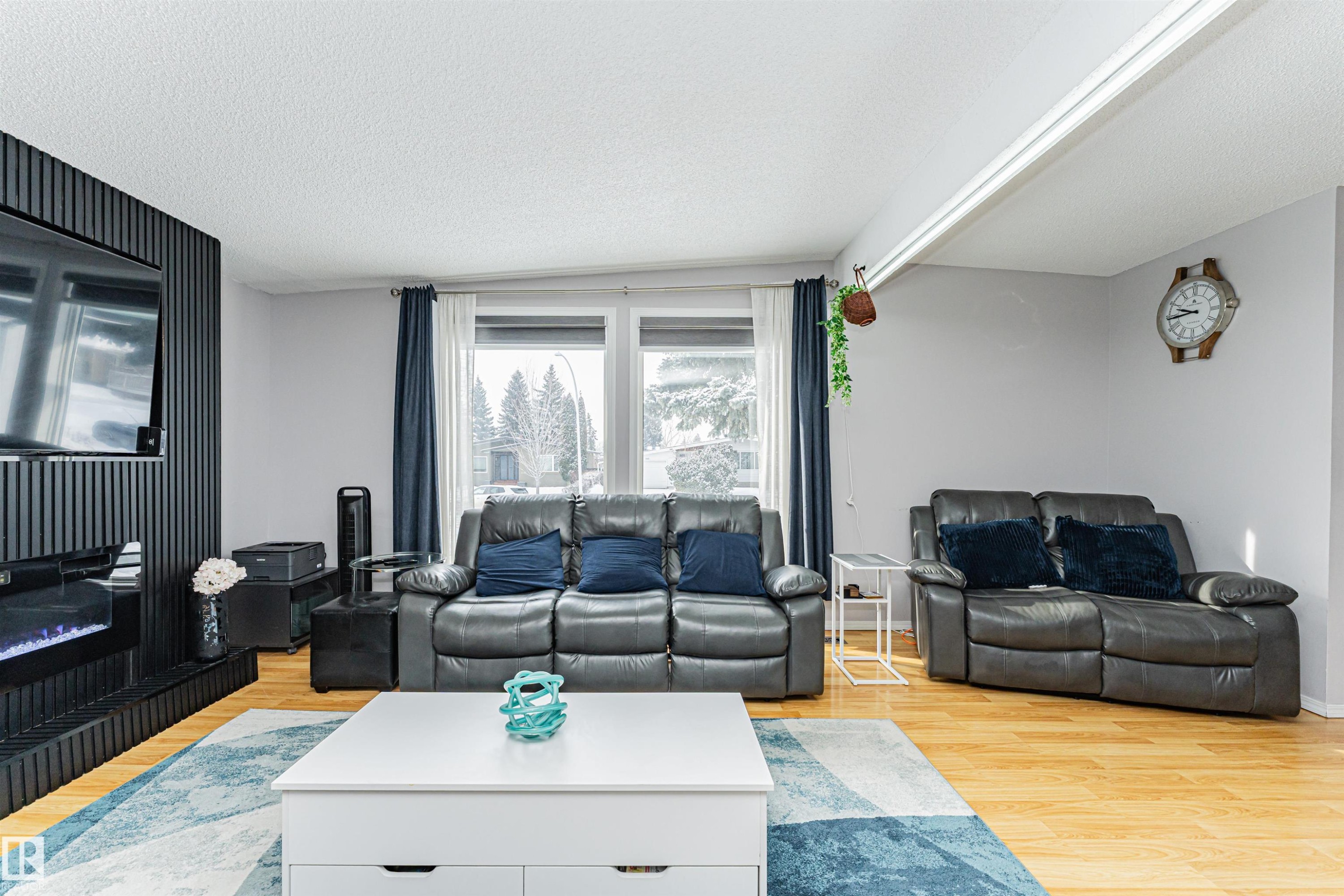 The living area features hardwood floors, a modern black accent wall with an integrated fireplace, and a large window providing natural light - 10412 39 Avenue, Edmonton, AB - Indoor Photo Showing Living Room