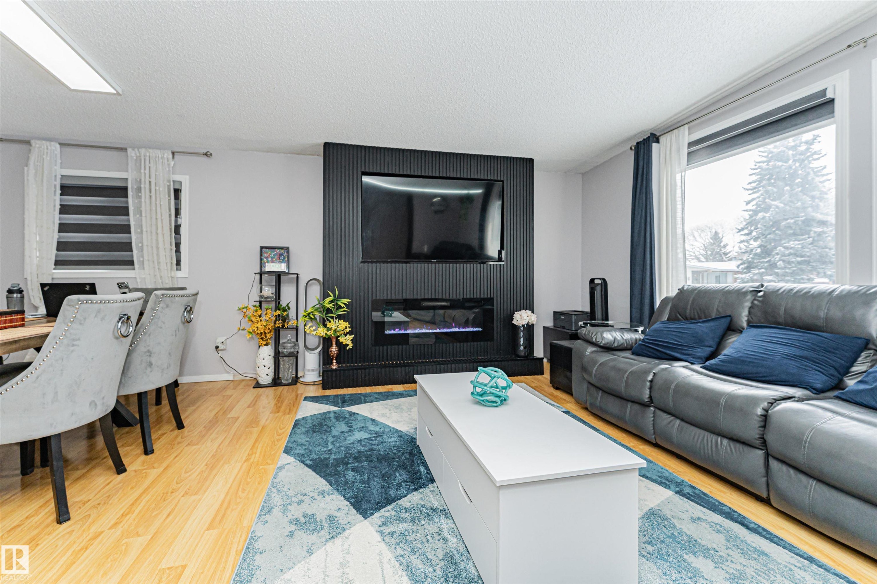 Living area featuring light wood flooring and a large window providing natural light - 10412 39 Avenue, Edmonton, AB - Indoor Photo Showing Living Room With Fireplace